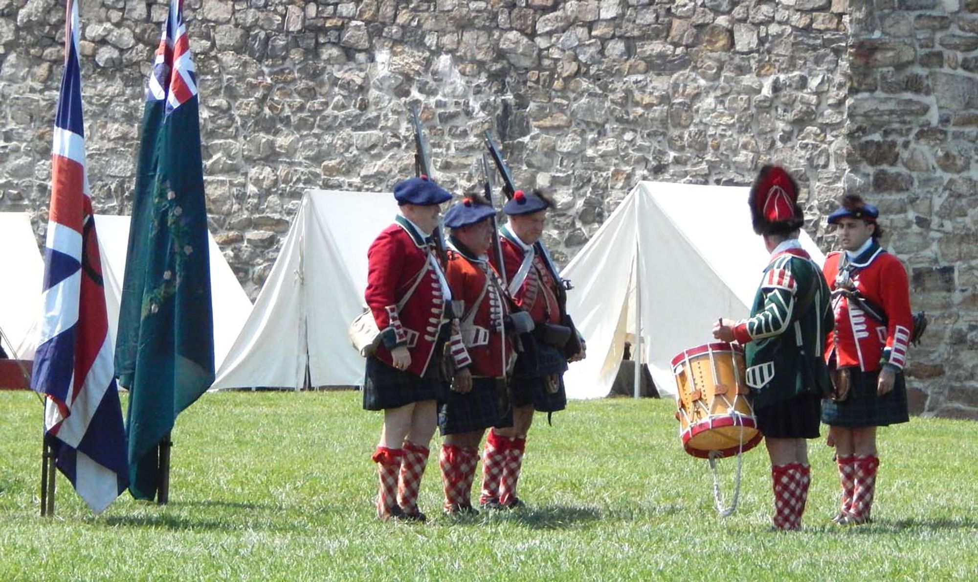 The small contingent of Highlanders assembles near their camp. Flats stand on the left, denoting their units, with three red-coated, Black-Watch-kilted soldiers wearing Tam O’Shanters standing center, with a drummer and officer to the right.