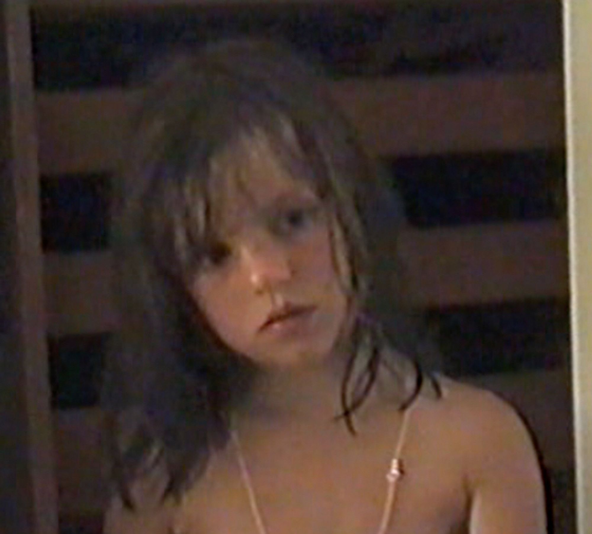 A screenshot from a home video from the 1990s with a 6 years old girl (me) with cute facial features but very sad eyes, wearing mom’s golden chain on bare shoulders. He head is leaning left and eyes are looking the opposite direction. She’s too serious for her age, probably neurodivergent.