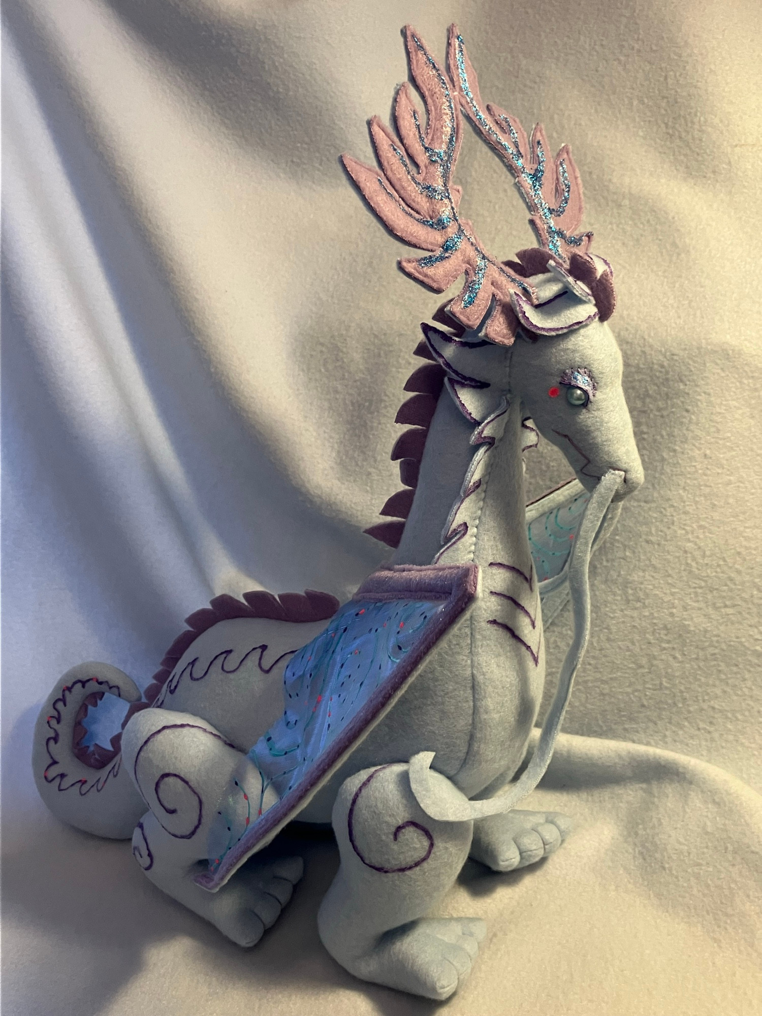 A light blue handsewn dragon with purple antlers and gossamer wings