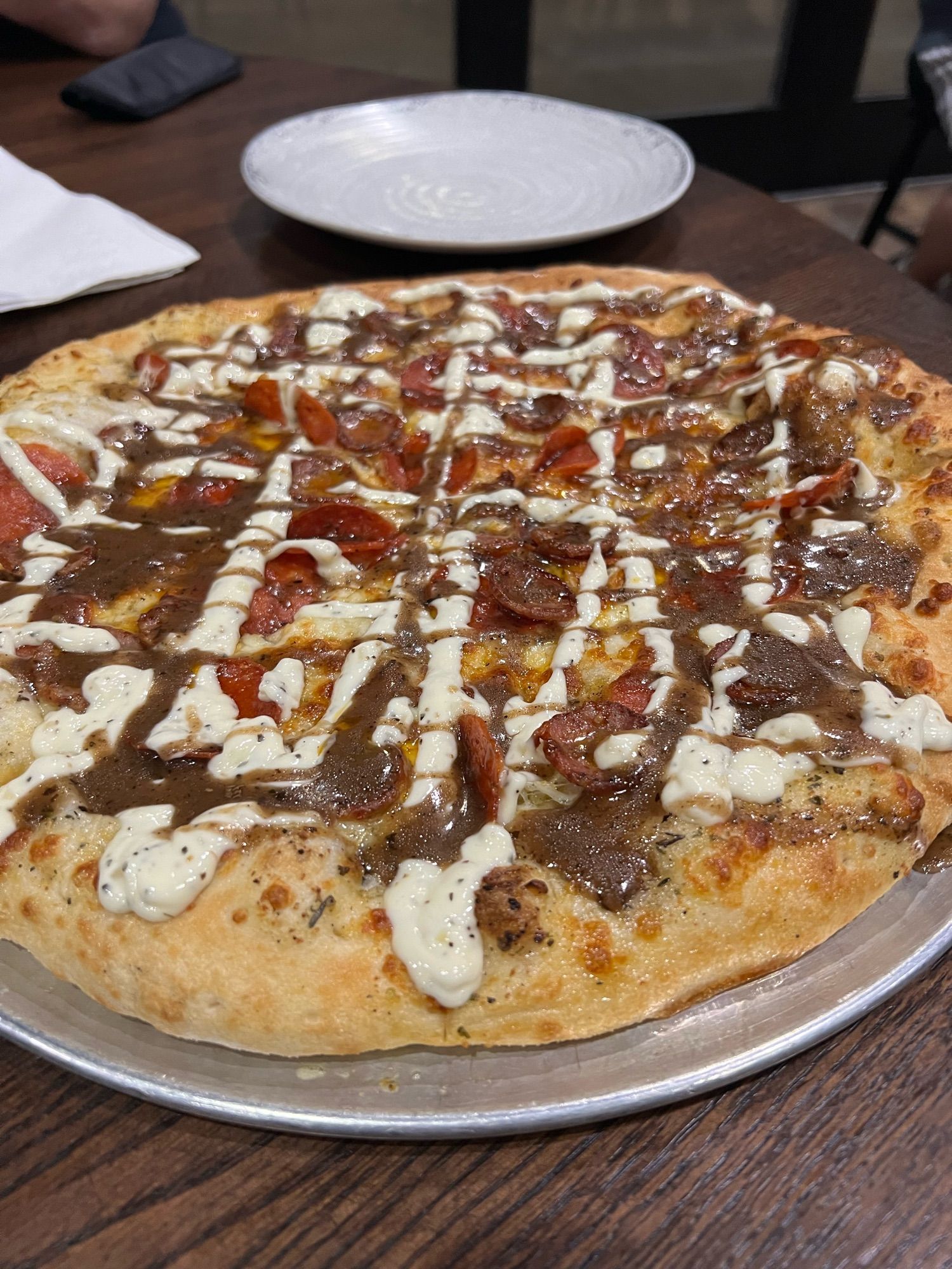 A pizza with mozzarella, pepperoni, sausage, garlic aioli and balsamic reduction.