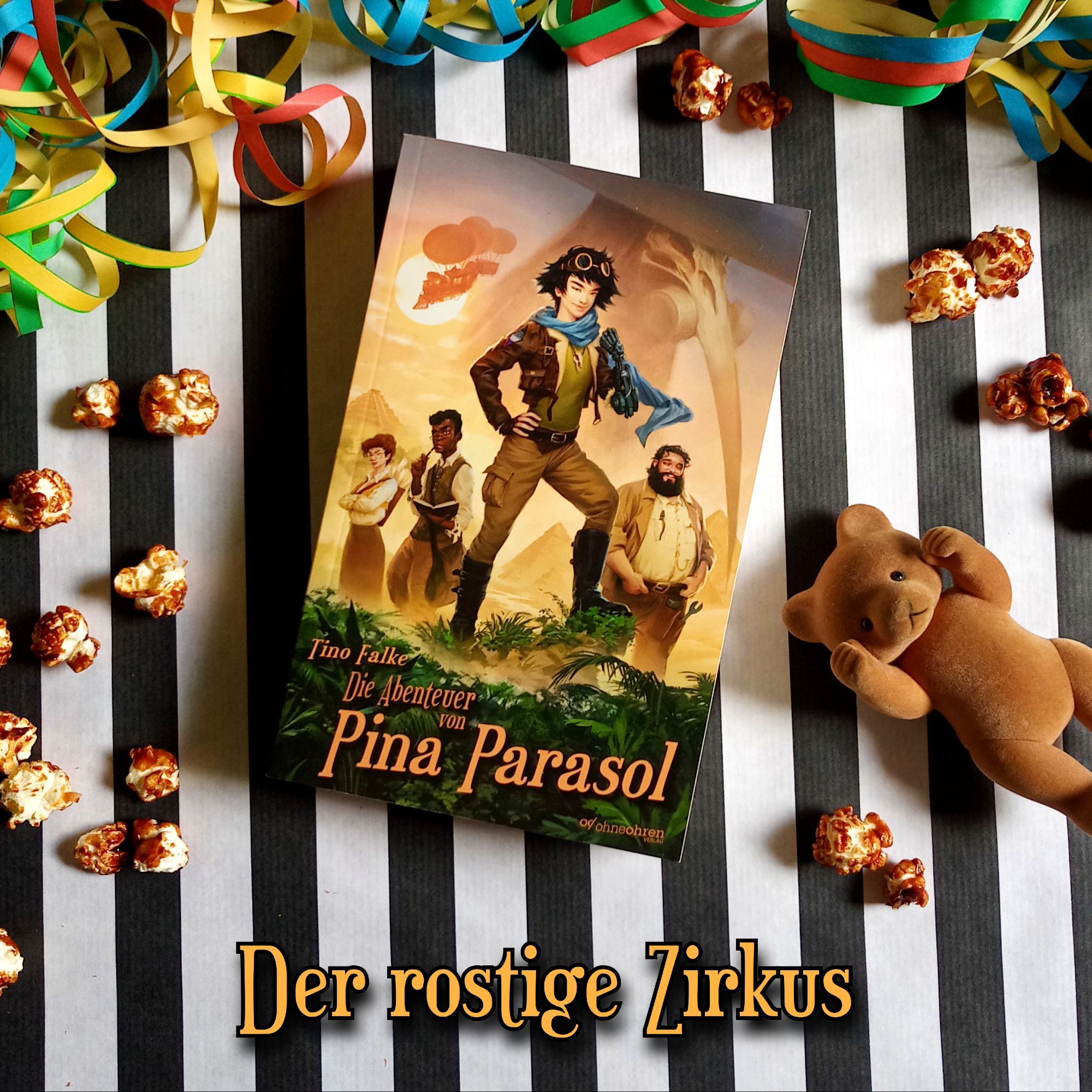 Foto vom Buch „Die Abenteuer von Pina Parasol“ vor schwarz-weiß gestreiftem Hintergrund. Rund um das Buch liegt Popcorn, bunte Luftschlangen und eine kleine Bärenfigur. Darunter steht in Braun: „Der rostige Zirkus“.