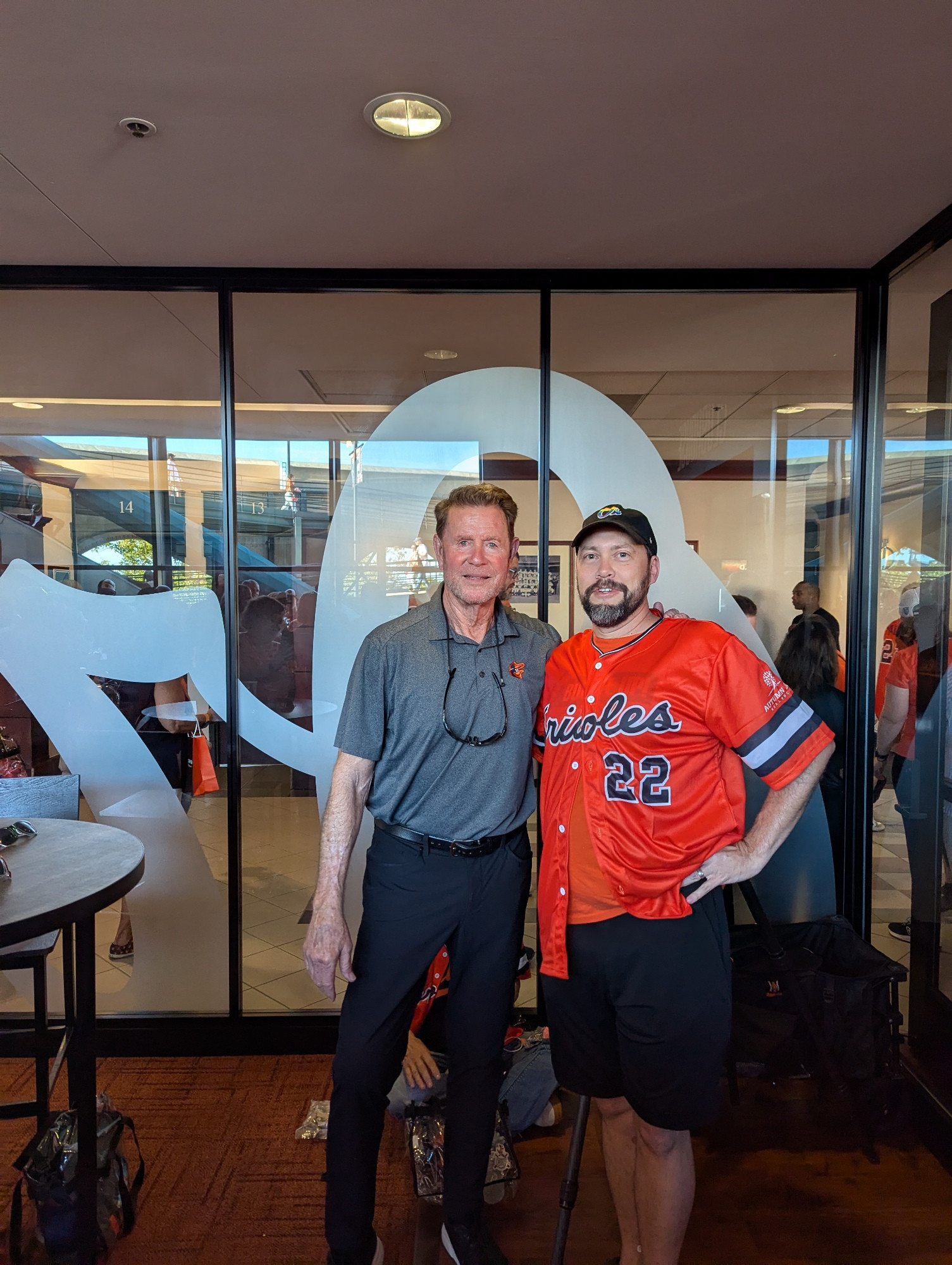 Jim Palmer (in gray Orioles polo shirt and black pants) stands next to me (43 year old white guy with dark brown and gray beard, wearing black O's pride cap, orange Jim Palmer replica jersey, and black shorts).