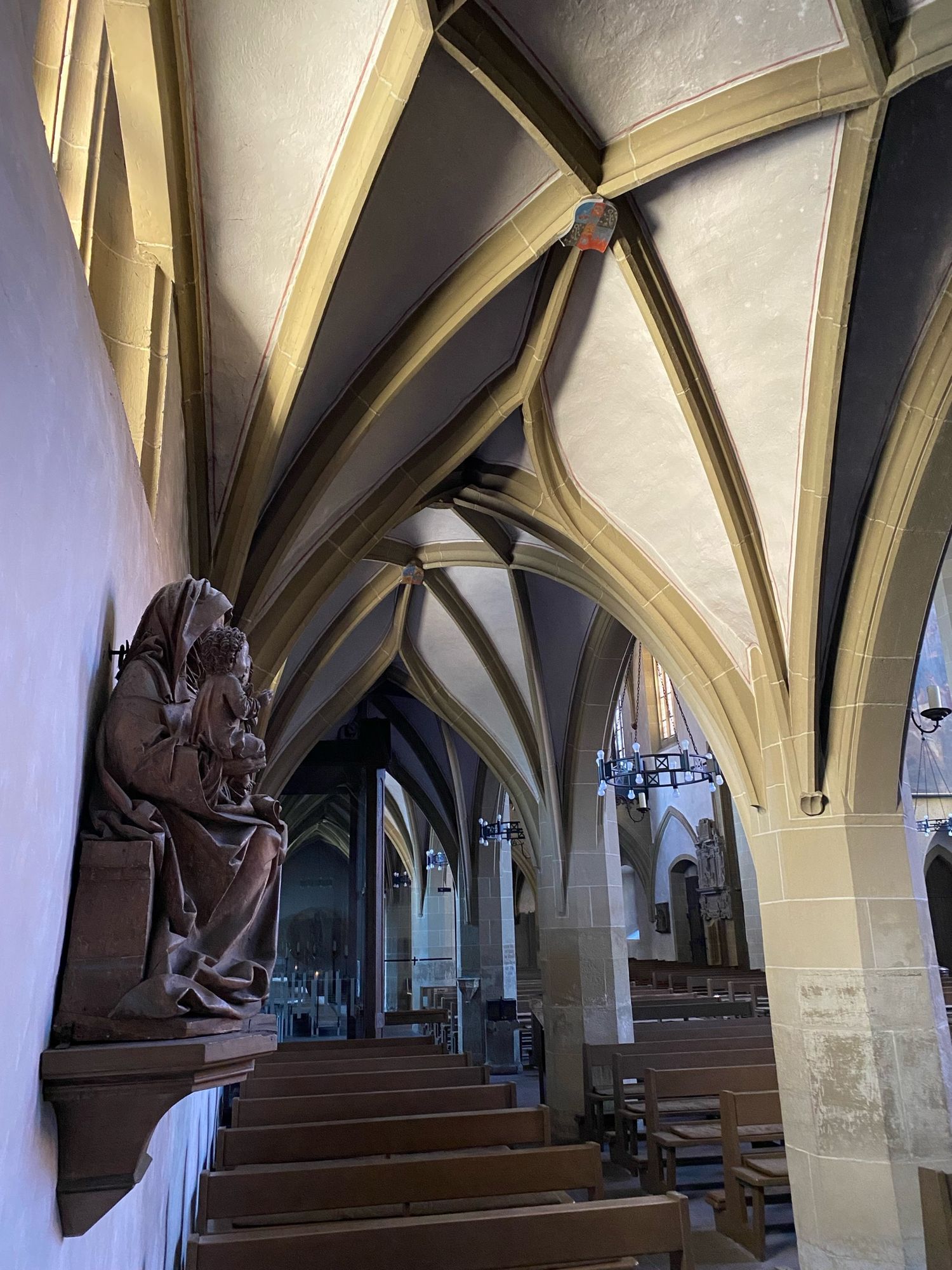 Niederes, schmales Kreuzrippengewölbe mit geschwungenen Formen. An de Wand eine sitzende Madonna mit Kind aus rötlichem Stein. Darunter Holzbänke.