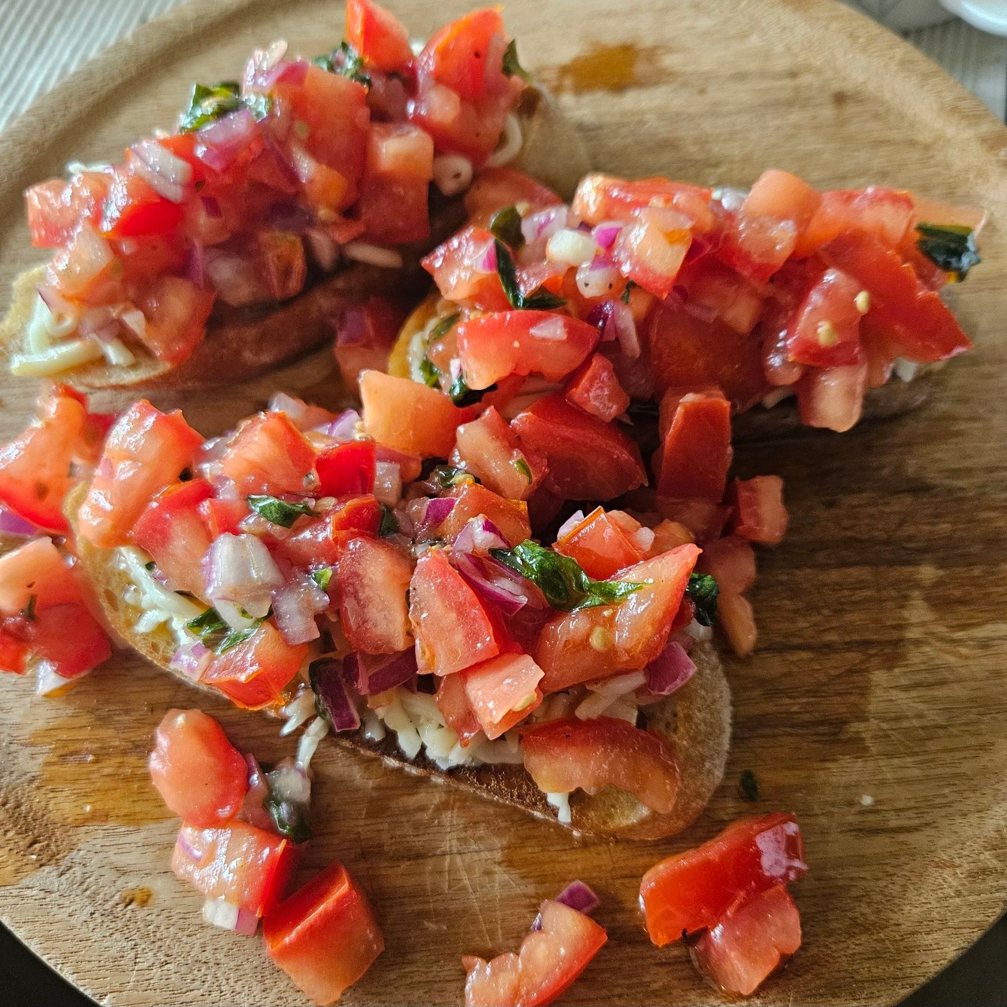 3 Stück Bruschetta mit reichlich Tomate auf einem Holzbrettchen.