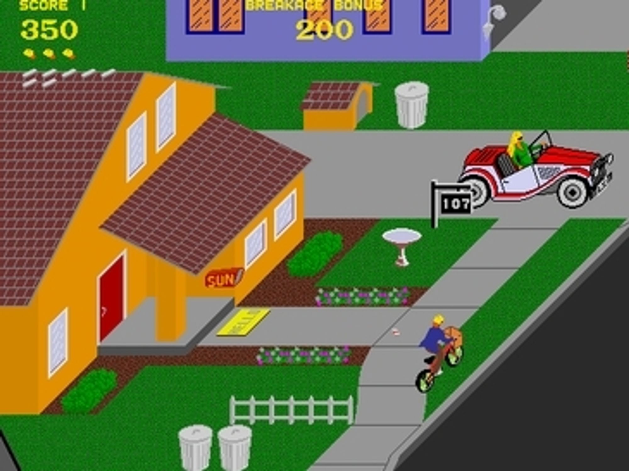 A screenshot from the Paperboy arcade game. A boy on a bicycle is shown on a sidewalk. He is pedaling past a house which he will need to toss a newspaper into the home's yard or on it's porch. He is pedaling toward a women in a convertible car. If he isn't careful to avoid her he will wreck his bike and lose a life in the game.