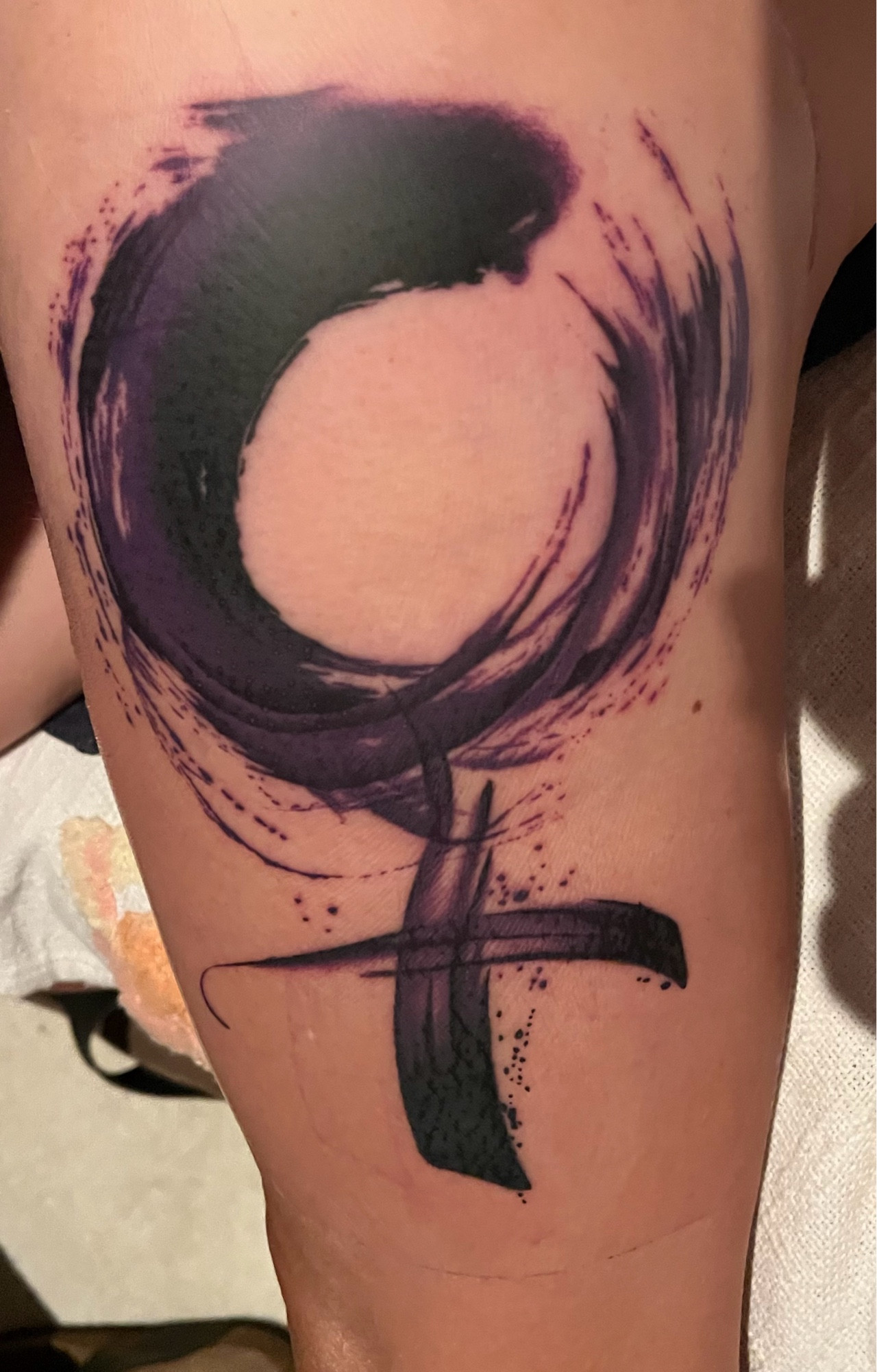 A thigh tattoo of the woman symbol in purple and black in a brushstroke style.