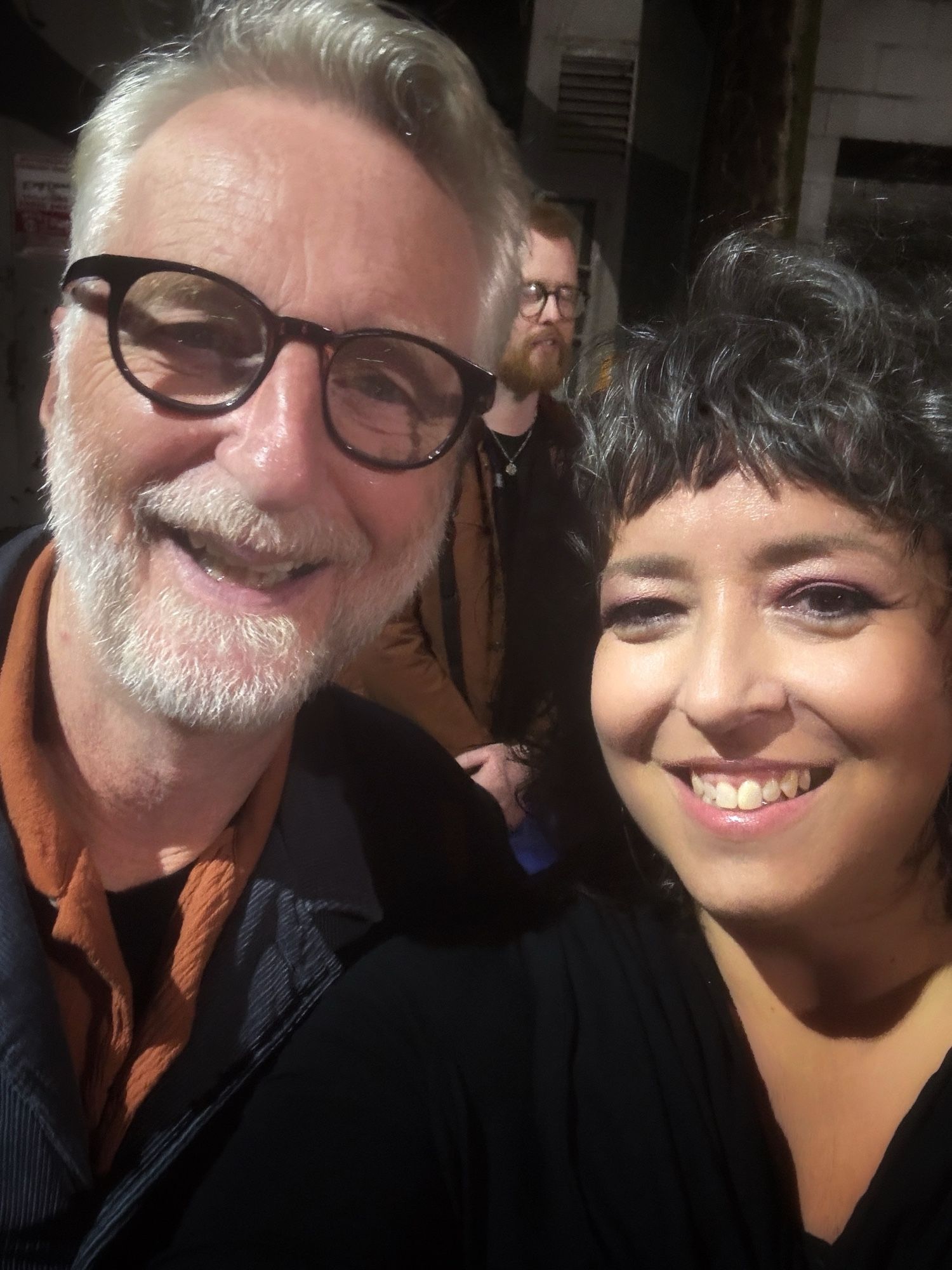 A head shot of two people in the photo. On the least is a Caucasian male in his early 60s with black glasses and a white short beard, smiling. On the right is a middle-aged Caucasian woman with brown hair smiling.