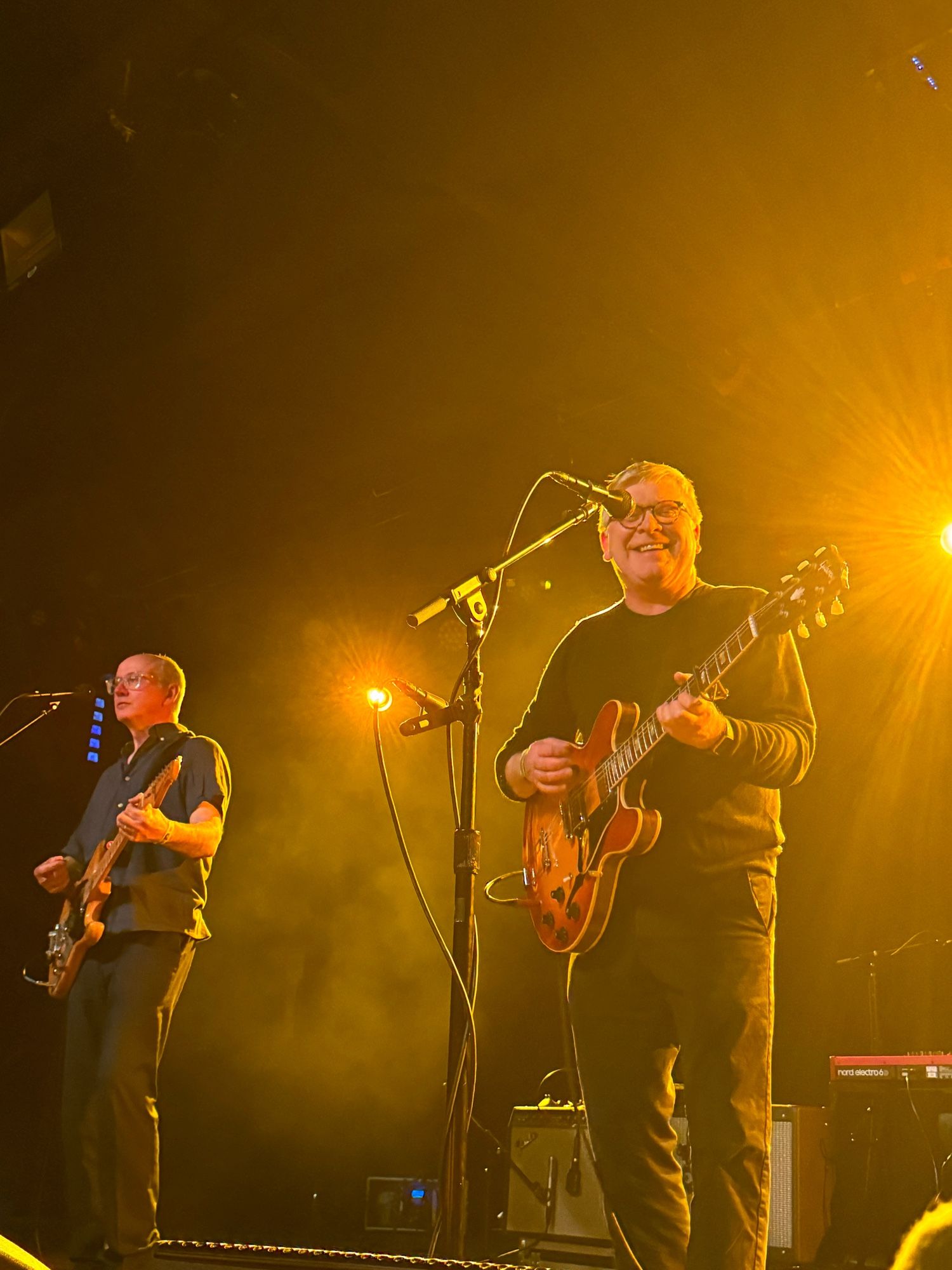 Photo of two Caucasian male members of Scottish band Teenage Fanclub, each with guitars, on stage in Seattle. One member, at right, is smiling.