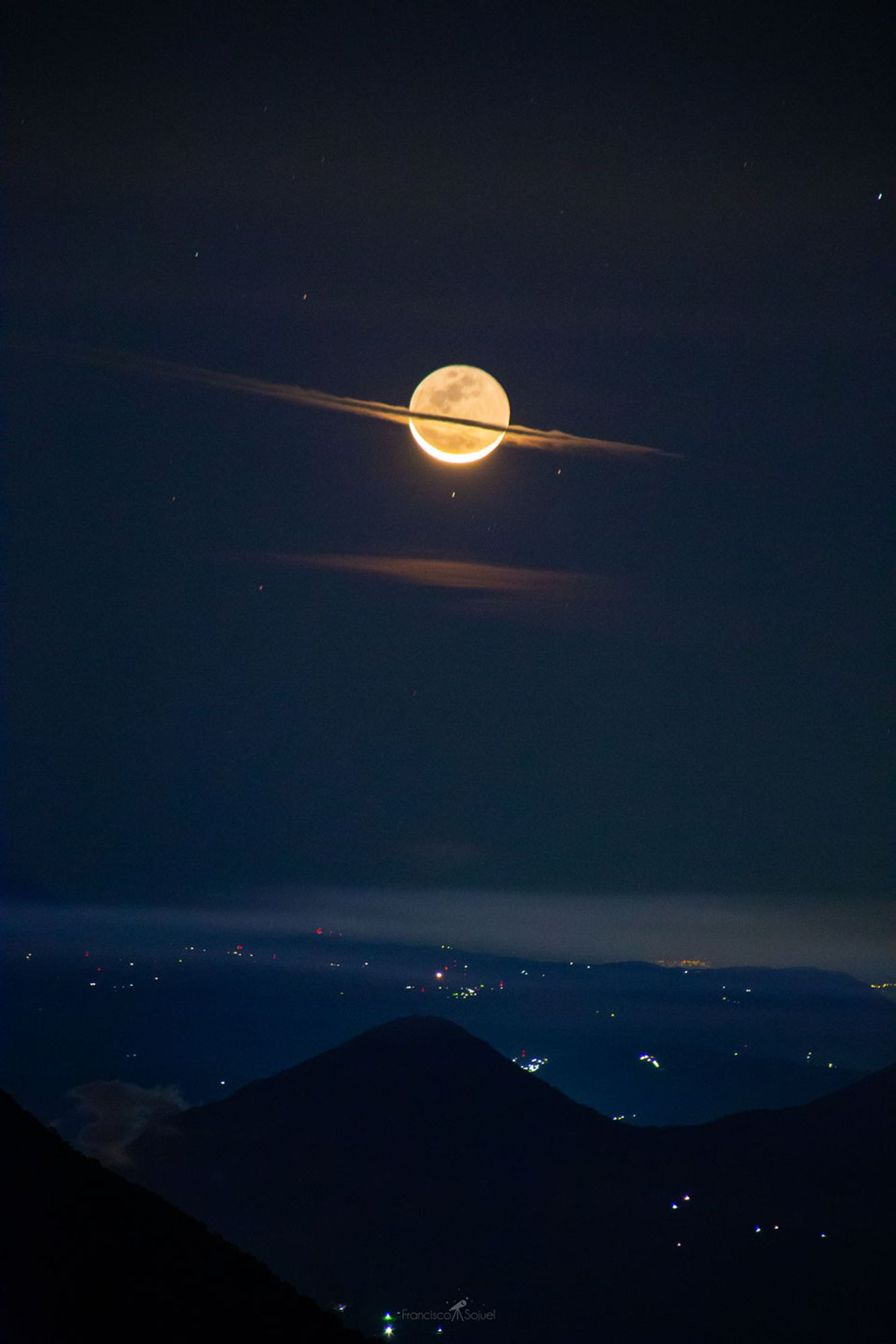 Why does Saturn appear so big? It doesn't -- what is pictured are foreground clouds on Earth crossing in front of the Moon. The Moon shows a slight crescent phase with most of its surface visible by reflected Earthlight, known as Da Vinci glow. The Sun directly illuminates the brightly lit lunar crescent from the bottom, which means that the Sun must be below the horizon and so the image was taken before sunrise.  This double take-inducing picture was captured on 2019 December 24, two days before the Moon slid in front of the Sun to create a solar eclipse. In the foreground, lights from small Guatemalan towns are visible behind the huge volcano Pacaya.    Your Sky Surprise: What picture did APOD feature on your birthday? (post 1995)