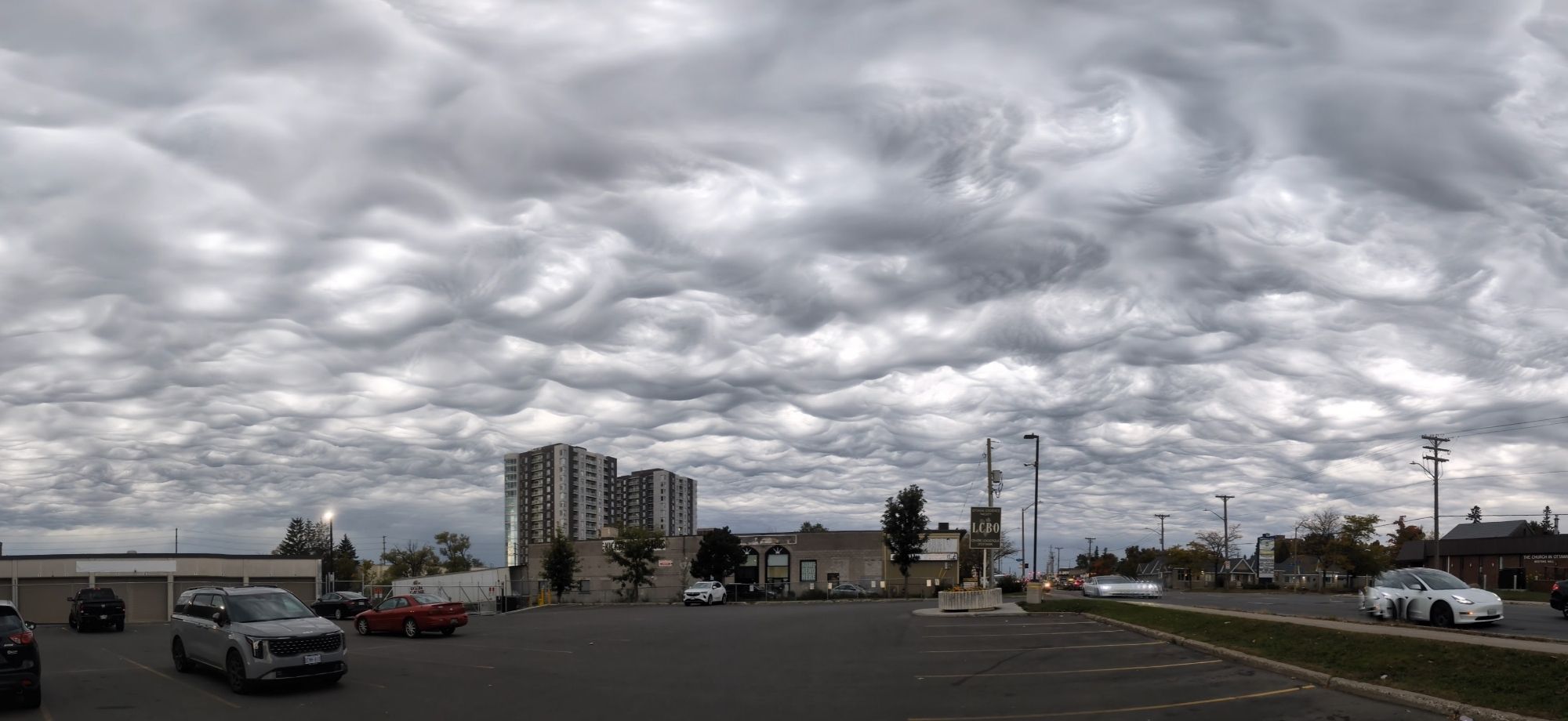 Dramatic asperatus clouds over a parking lot look like the bottom of waves, but they're not in lines. The tops are white and the bottoms are dark. Looks like a special effect from Ghostbusters.