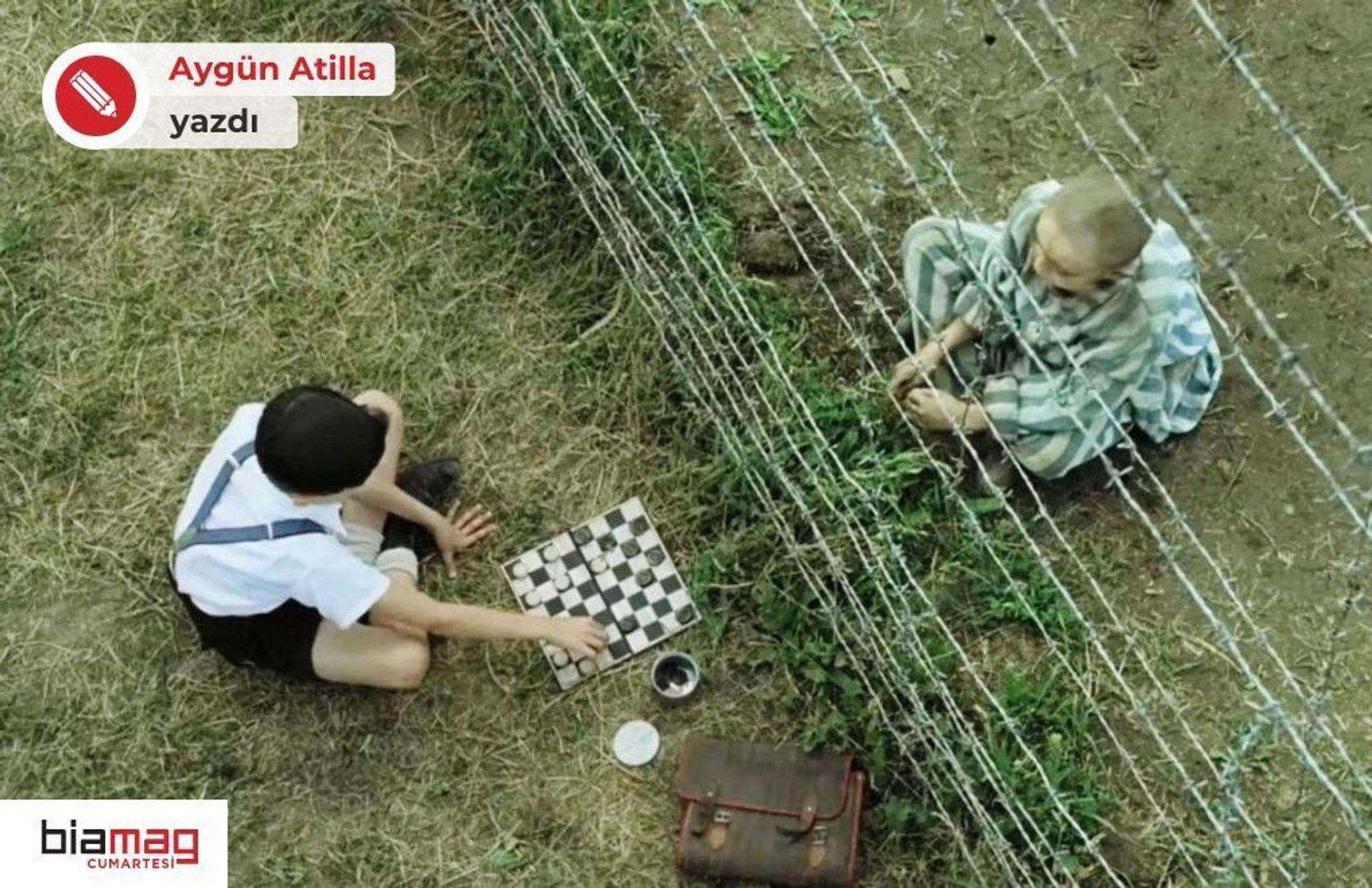 Görselde iki çocuk var, aralarında dikenli bir tel örgüyle ayrılmışlar. Soldaki çocuk açık renk bir gömlek ve koyu renk pantolon giymiş, yerde oturuyor. Önünde bir dama tahtası bulunuyor ve oyun oynuyor gibi görünüyor. Sağdaki çocuk ise çelimsiz ve başı tıraşlı, üstünde ise çizgili bir giysi var, bu kıyafet Nazi toplama kamplarında tutulanların giydiği üniformalara benziyor. O da tel örgünün diğer tarafında oturuyor, ve elleriyle yerdeki otlarla oynuyor gibi.  Bu görüntü, iki çocuğun arasındaki masumiyetin ve savaşın, esaretin getirdiği acımasızlığın çarpıcı bir sembolü. Çocuklardan biri özgürken diğeri hapsedilmiş, fakat tel örgünün iki yanındaki masumiyetin karşı karşıya gelişi dramatik bir sahne yaratıyor.