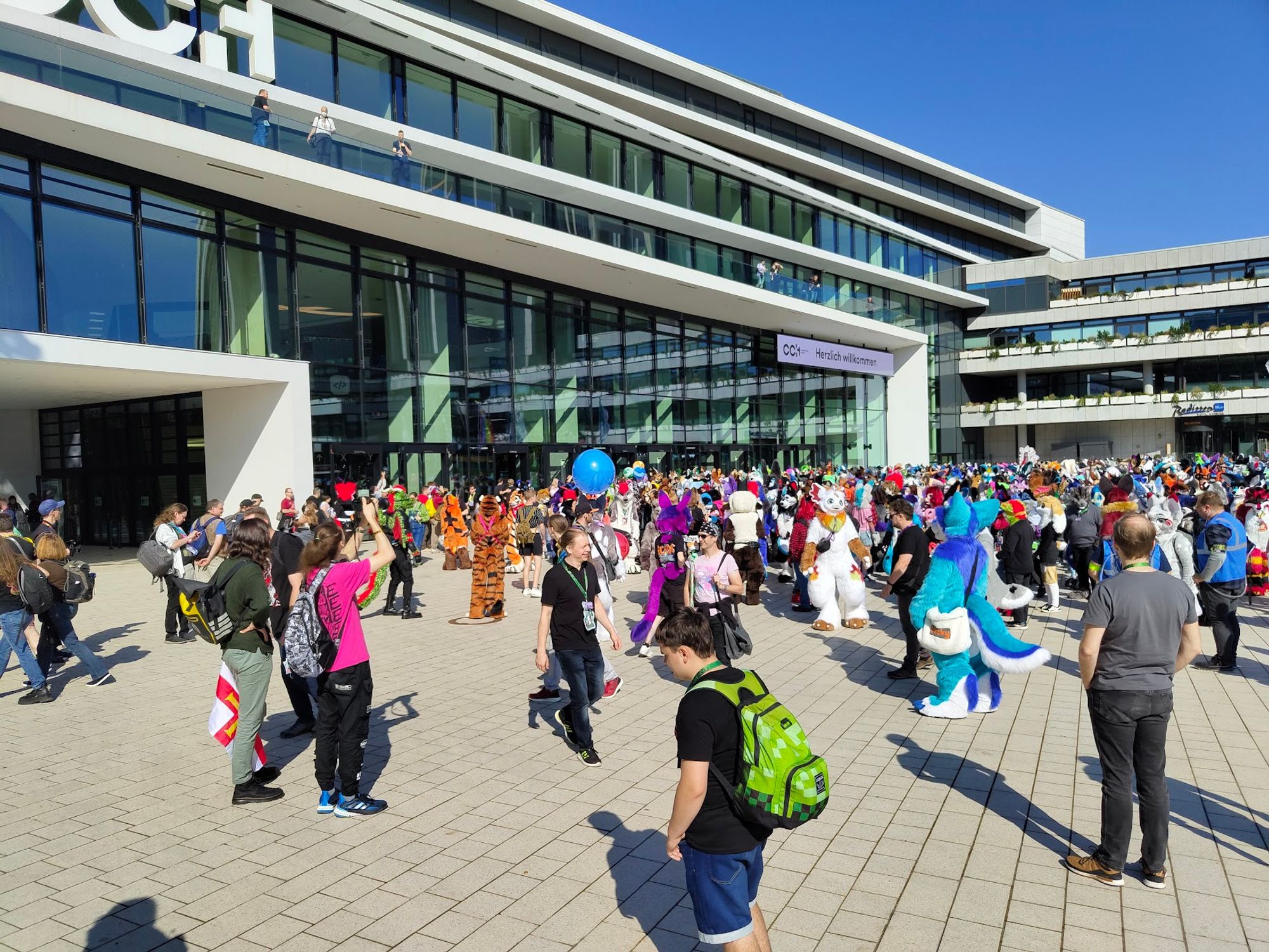 A bunch of furries in fursuit on the CCH plaza. Most are facing the CCH and looking up to the photographer ahead of the Fursuit Group Photo on Saturday.