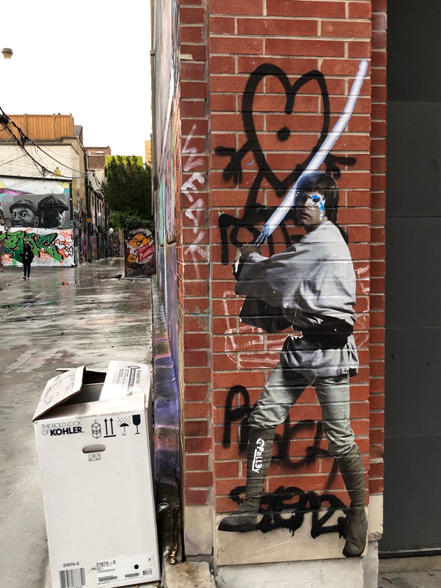 Luke Skywalker by Palley @pall3y
A pasteup of Luke Skywalker with spray painted white lightsaber that looks like it’s glowing, from the original Star Wars. It’s on a red brick pillar and Graffiti Alley can be seen to the left of it.