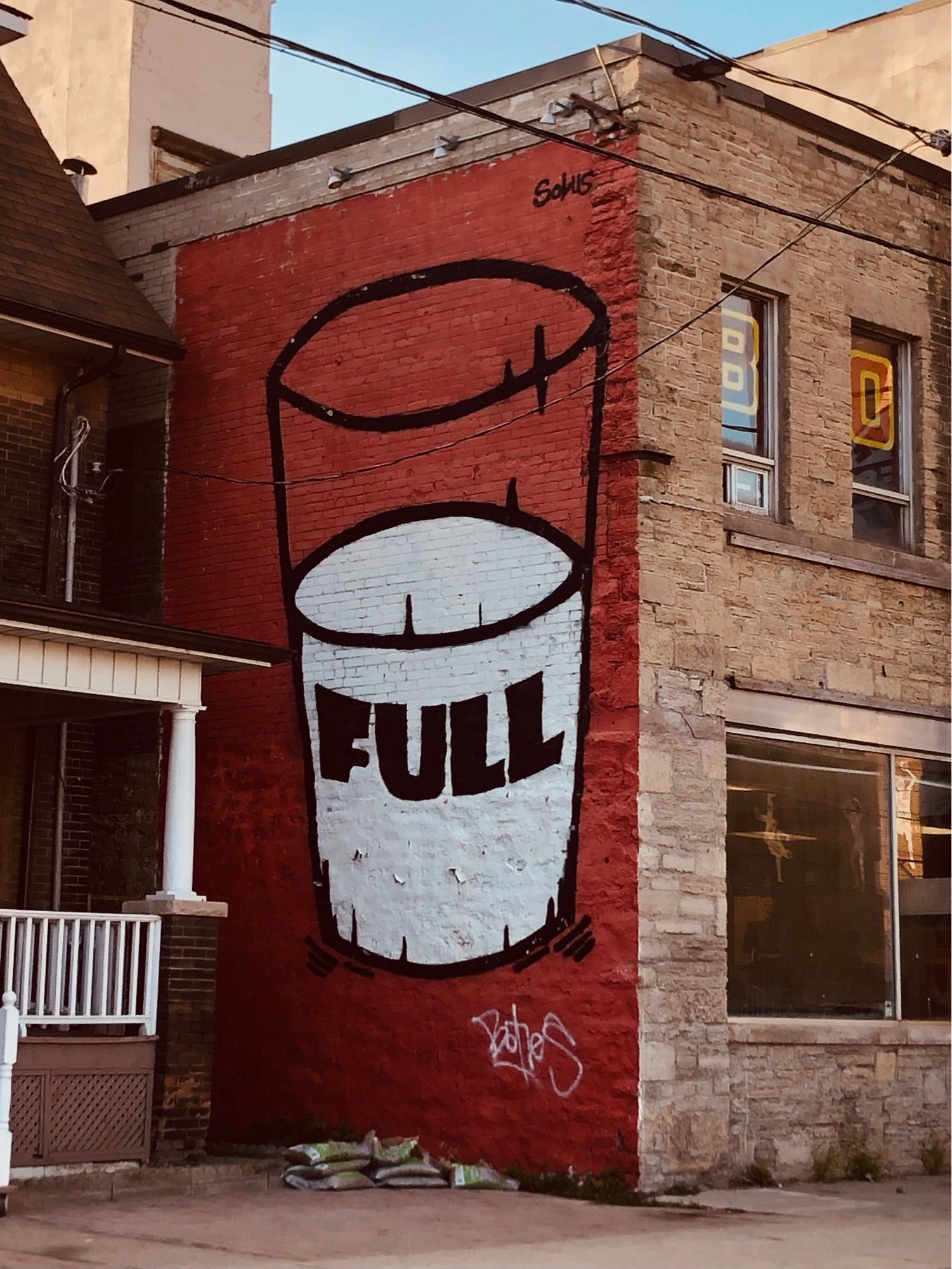 Street art on the side of a 2-storey building in Toronto, on Dundas & Bloor. A black outline of a tall milkglass half-filled with milk on a solid red background. The word ‘FULL’ in thick black type is on the milk, curved around the shape of the glass.