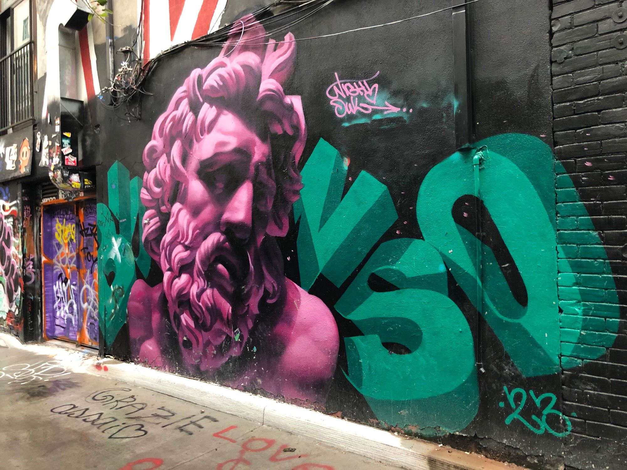 A black wall with a bright pink and black portrait of bearded man with curly hair, face turned to 3/4 side profile, a sorrowful look on his face. In large 3D green letters with shading it spells BUNSO. 2023 By Night Owl Drawings / BUNSO