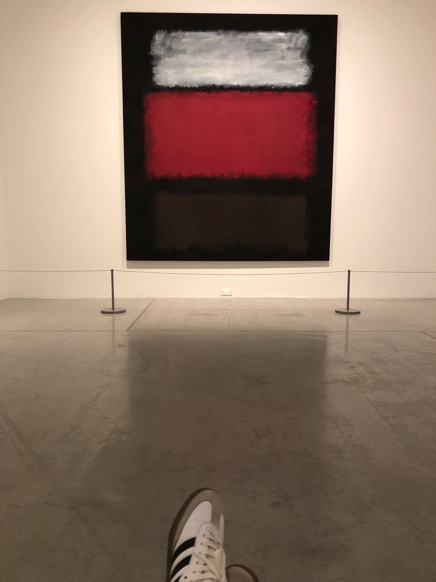 Mark Rothko’s ‘No.1, White and Red’ hanging on a white wall with my sneaker feet poking up at the bottom of the photo. It’s maybe 6’x 4 1/2’ with a messy looking white and light grey blurry rectangle above a larger red blurry rectangle above a black blurry rectangle, all on a darker black background.