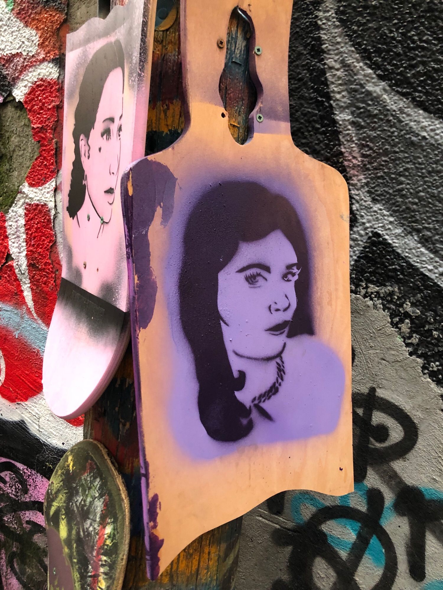 Black stencil on purple background of woman with long black hair looking flirty at the beholder of this art, wearing a chain necklace