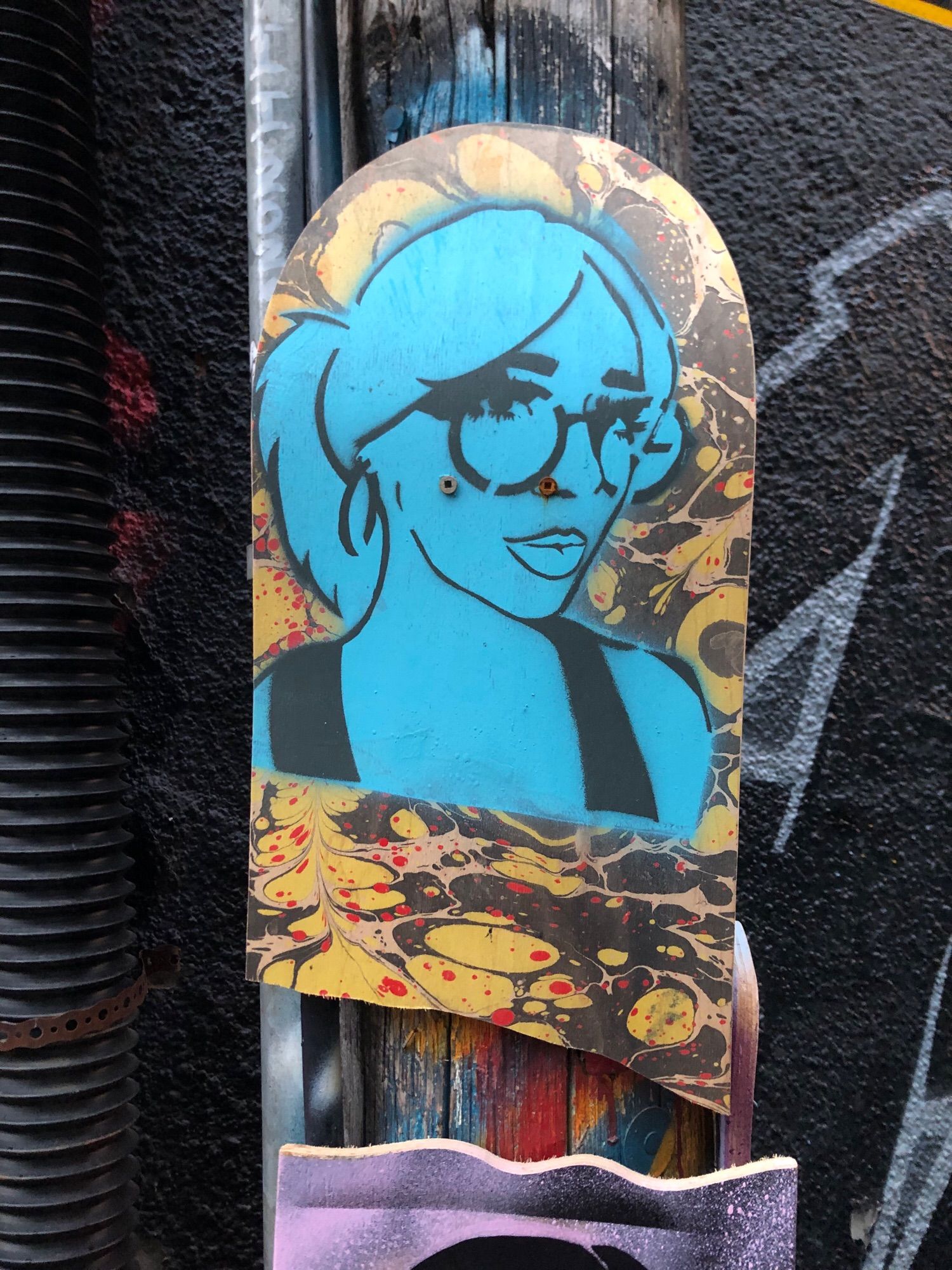 Black stencil of blue woman with round glasses, ponytail and pouty lips on half a skateboard that has a cool yellow and black circle design