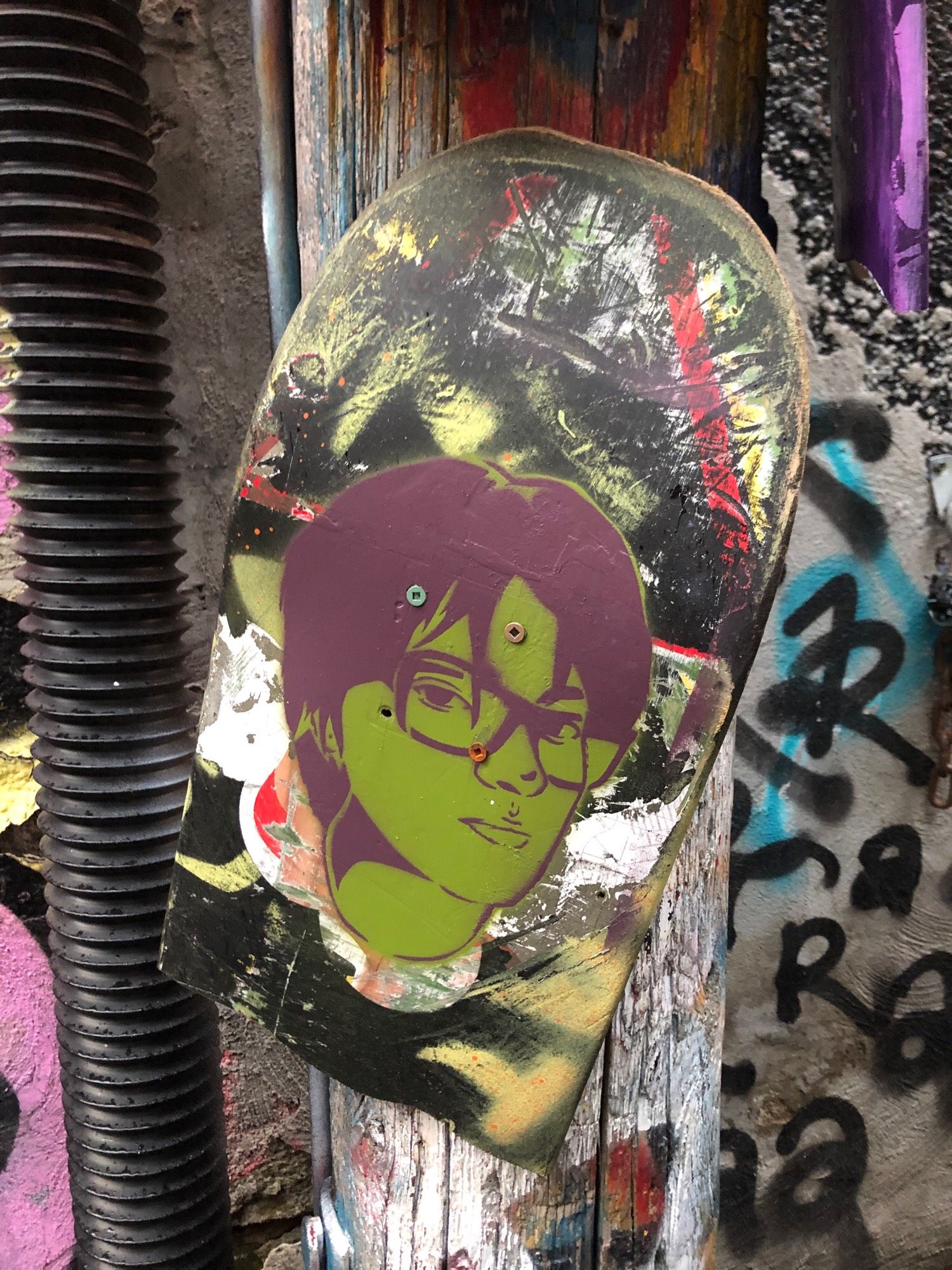 A dark brown or purplish stencil of an olive green person with short pixie hair and long pieces of bangs coming down in front of square eyeglasses and eyes looking right at you