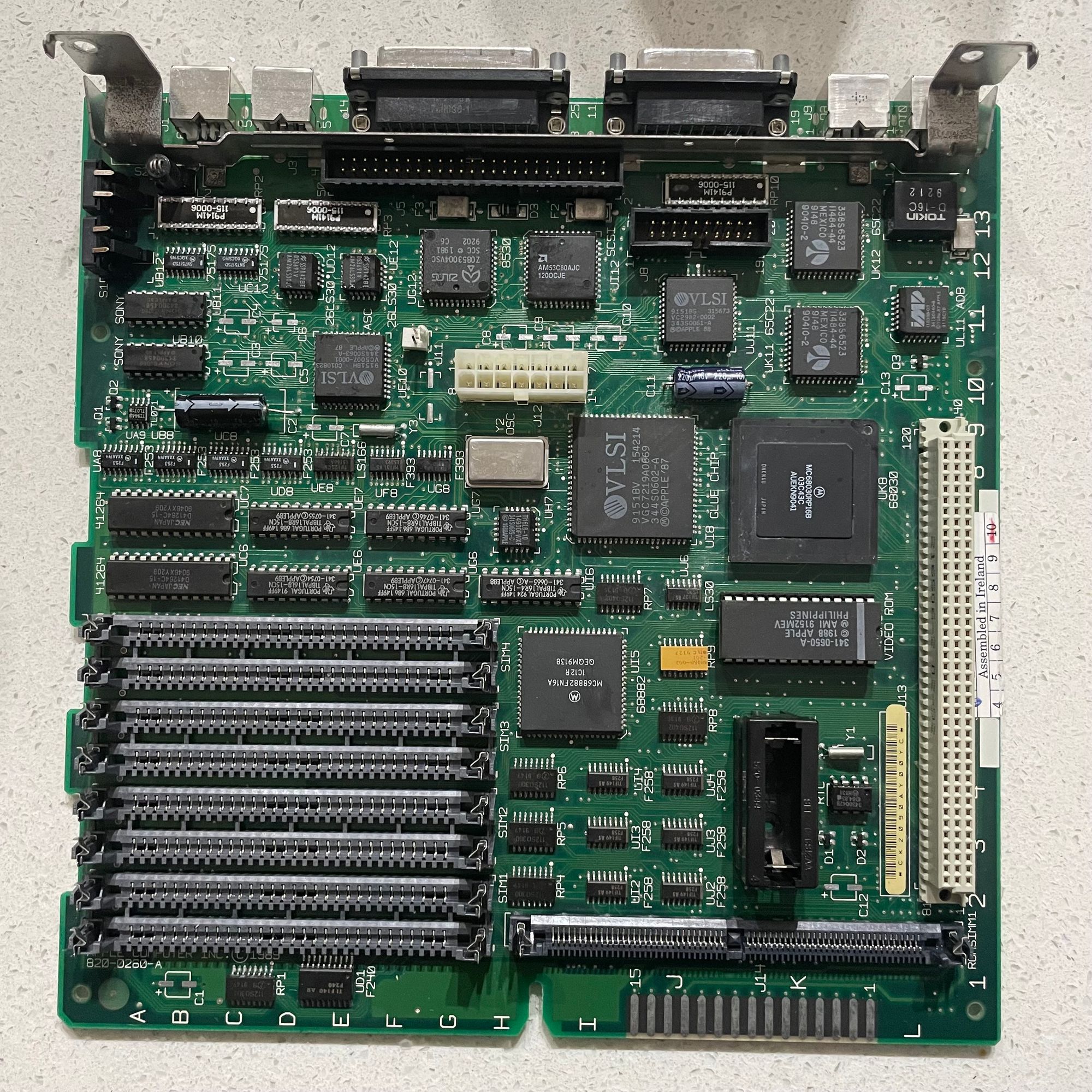 The top-down view of a Macintosh SE/30 logic board with bare silver pads where there were once leaky electrolytic capacitors.