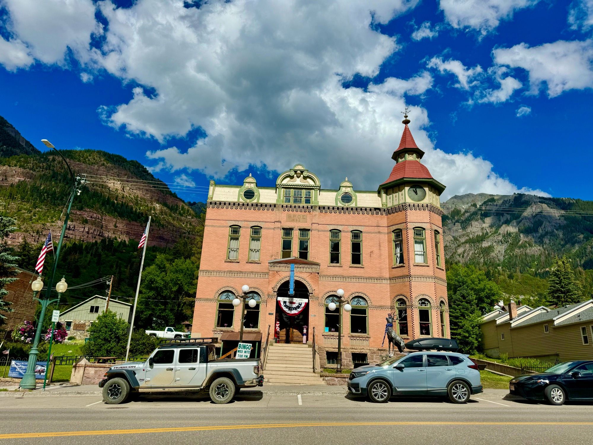 Facade of a historic building on a main street, with mountains in the background and a blue sky with clouds.