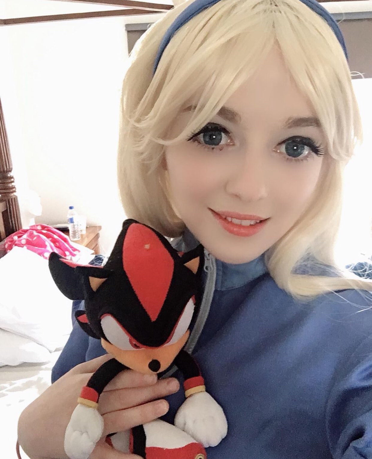 cosplay of maria robotnik from sonic the hedgehog. she has blonde hair and a blue shirt and holding a shadow plushie