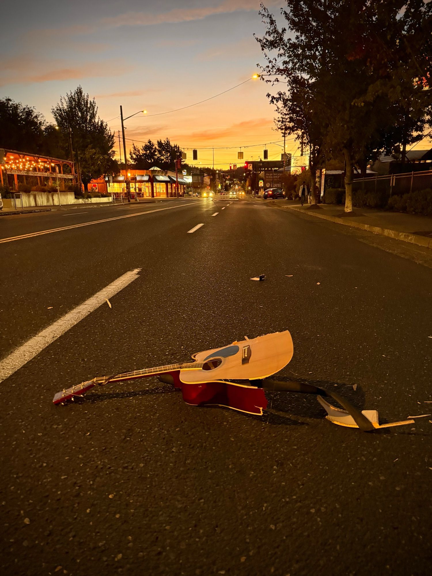 a photograph of a beautiful sunset and a smashed up guitar sitting in the middle of the street