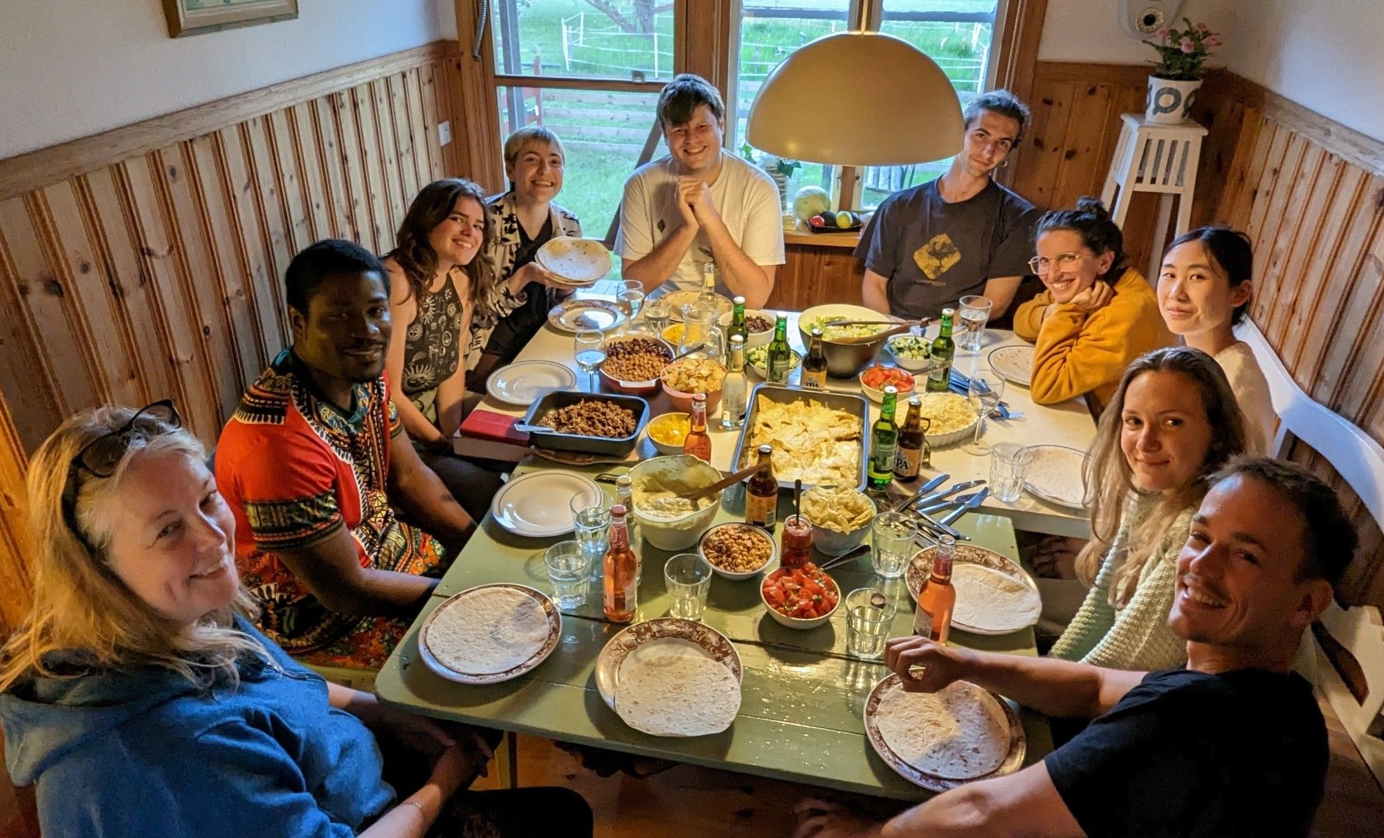 Students and researchers from the 2024 flycatcher monitoring field season sit around a table for dinner .