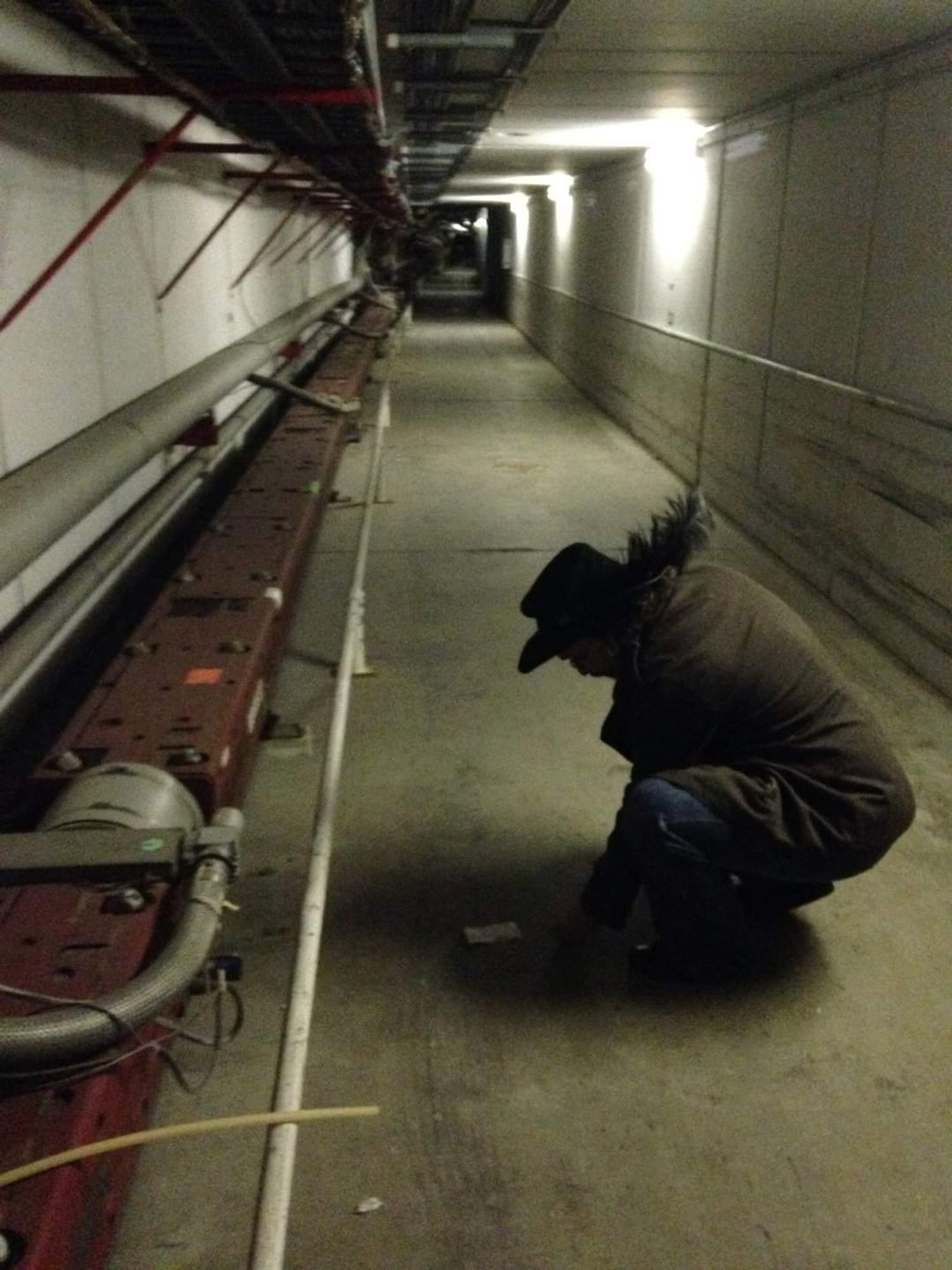 Poster crouching in a tunnel next to parts of a Fermi Lab's Tevatron.