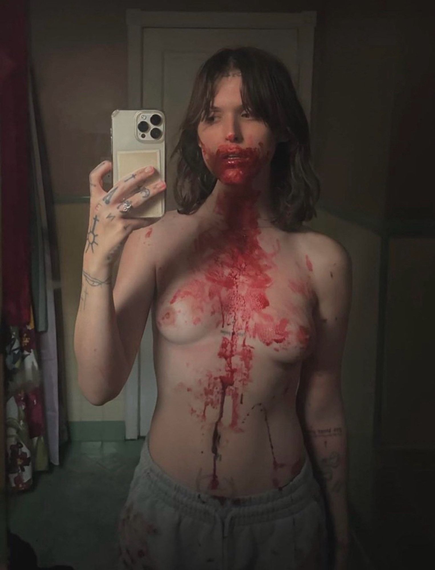 Ethel Cain topless in gray sweatpants with blood running down from her mouth onto her chest and abdomen