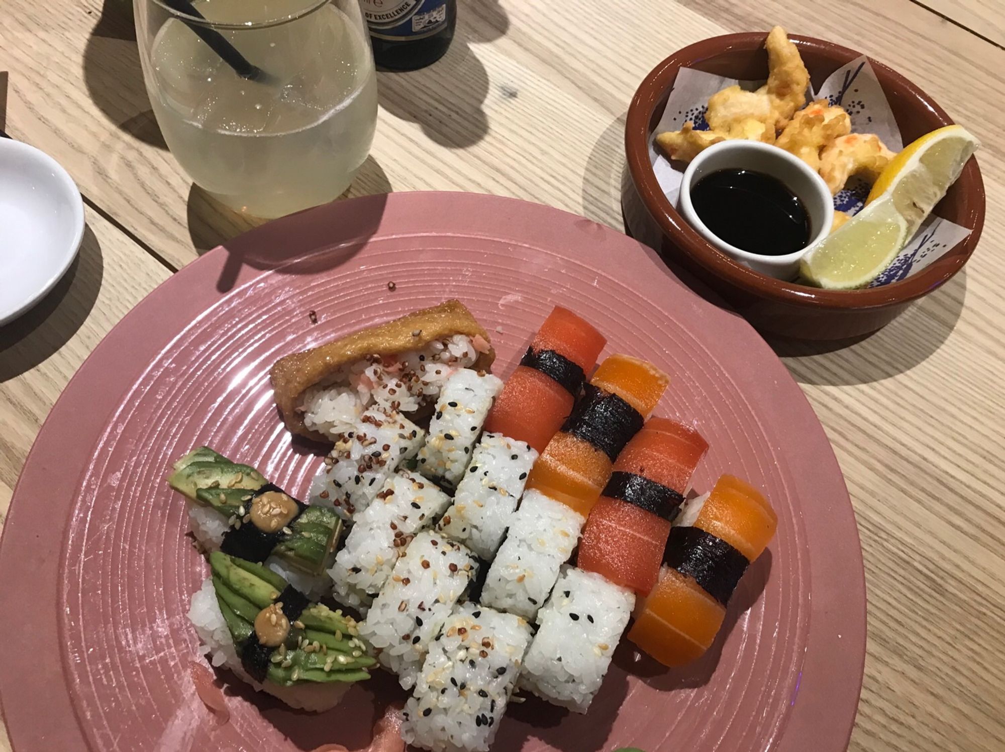 Eine vegane Sushi-Platte. 8 Inside Out-Maki, 1 Inari (Mit Reis gefüllte Tofutasche), 6 Nigiri, von denen 2 mit Lachsersatz, 2 mit Tunfischersatz und 2 mit Avocado sind. Daneben eine kleine Bowl mit 5 Stück Garnelenersatz, 2 Stück Zitrone und einem Schälchen Sojasoße.