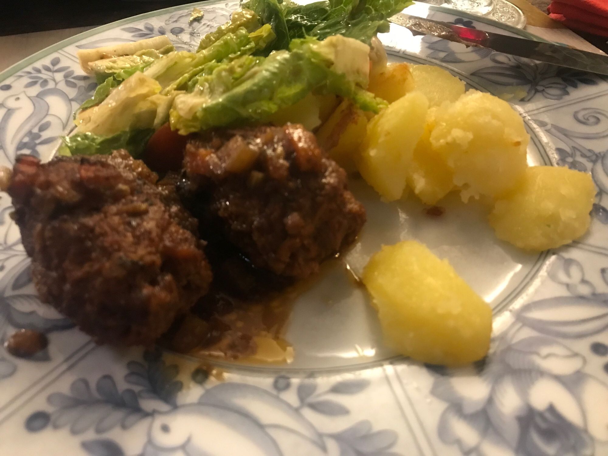 2 Kimchi-Rouladen in Gemüse-Rotwein-Sud mit 4 Stück Bratkartoffeln und etwas Salat auf einemit blauen Zeichnungen verziertem Teller.