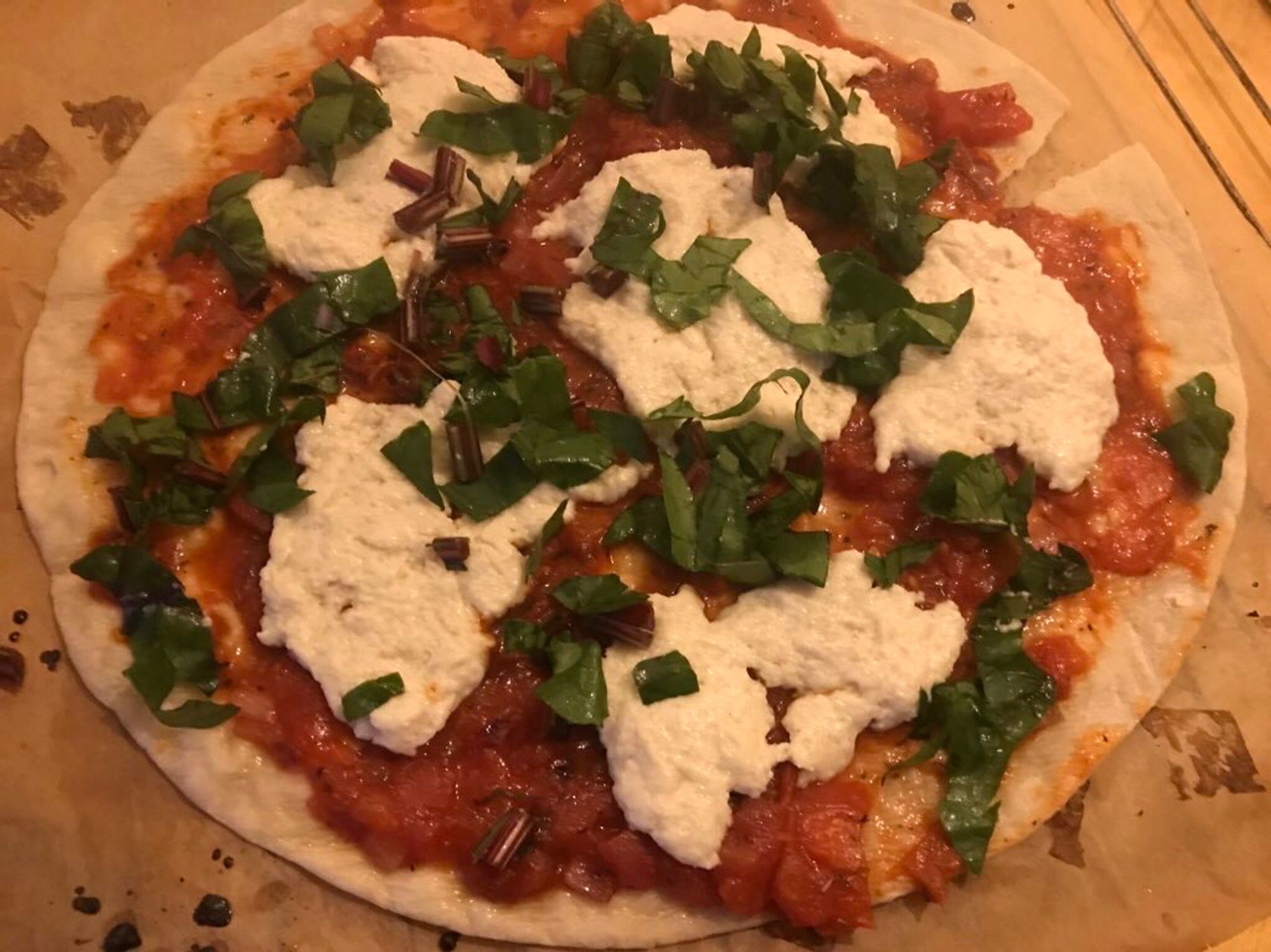 Pizza mit Tomatensoße, veganem Mozzarrella und Grünzeug.