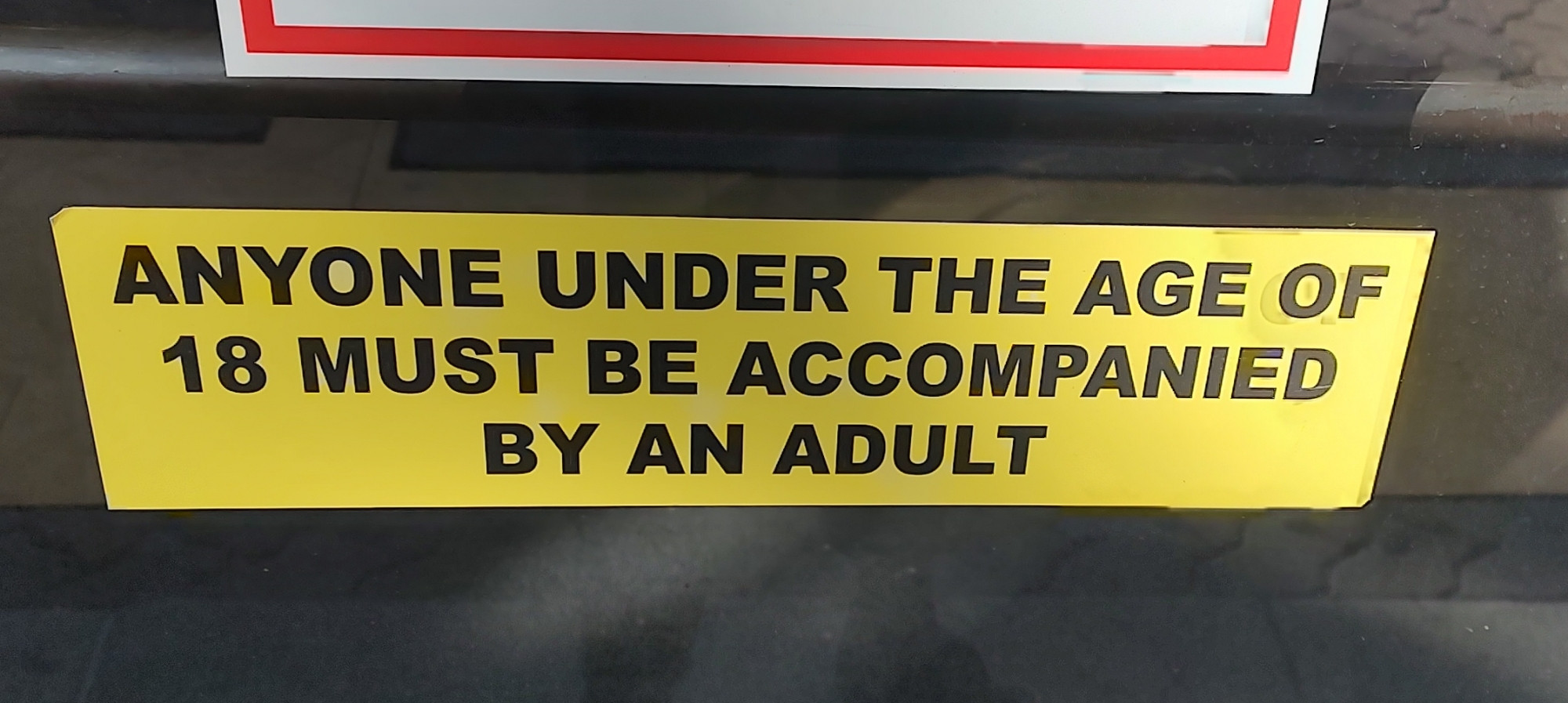 A sign on a door that reads "Anyone Under the Age of 18 Must be Accompanied By An Adult"