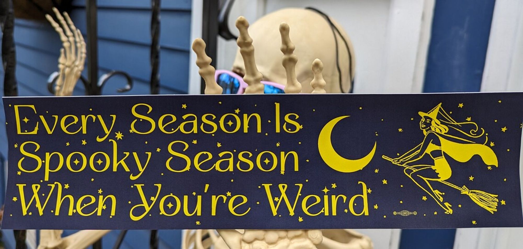 Photograph of a bumper sticker in midnight blue which reads, in yellow ornamented text,
Every Season Is 
Spooky Season
When You're Weird

Also in yellow is a crescent moon and a vintage illustration of a witch on a broom