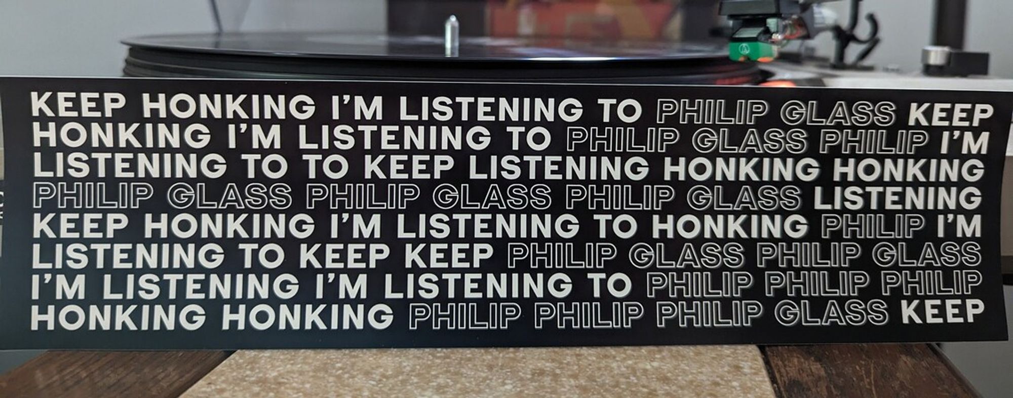 Black bumper sticker with white text reading
KEEP HONKING I'M LISTENING TO PHILIP GLESS KEEP HONKING I'M LISTENING TO PHILIP GLASS PHILIP I'M LISTENING TO TO KEEP LISTENING HONKING HONKING PHILIP GLASS PHILIP GLASS PHILIP GLASS LISTENING KEEP HONKING