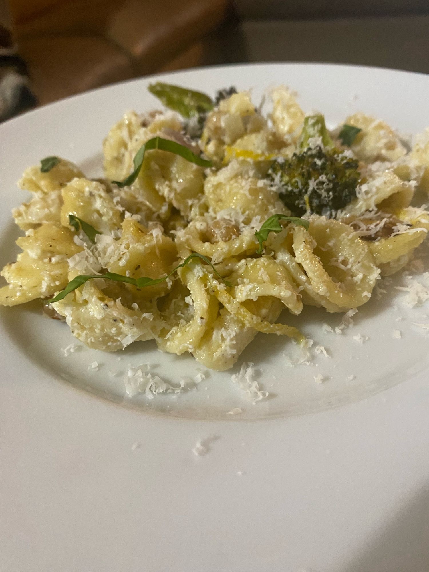 Orecchiette with roasted broccoli and chickpeas in garlic oil on white plate, garnished with Parmesan and strips of basil