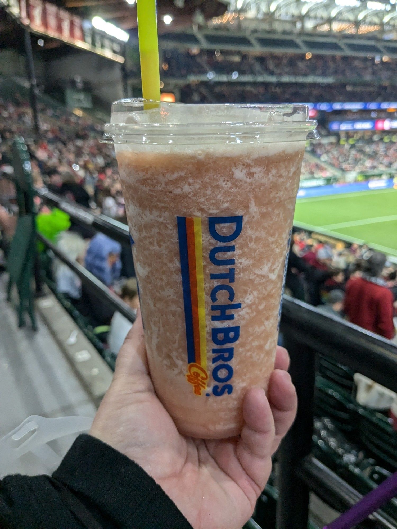 Close up of a plastic cup with a Dutch Bros strawberry smoothie. The blurry background is of Providence Park.