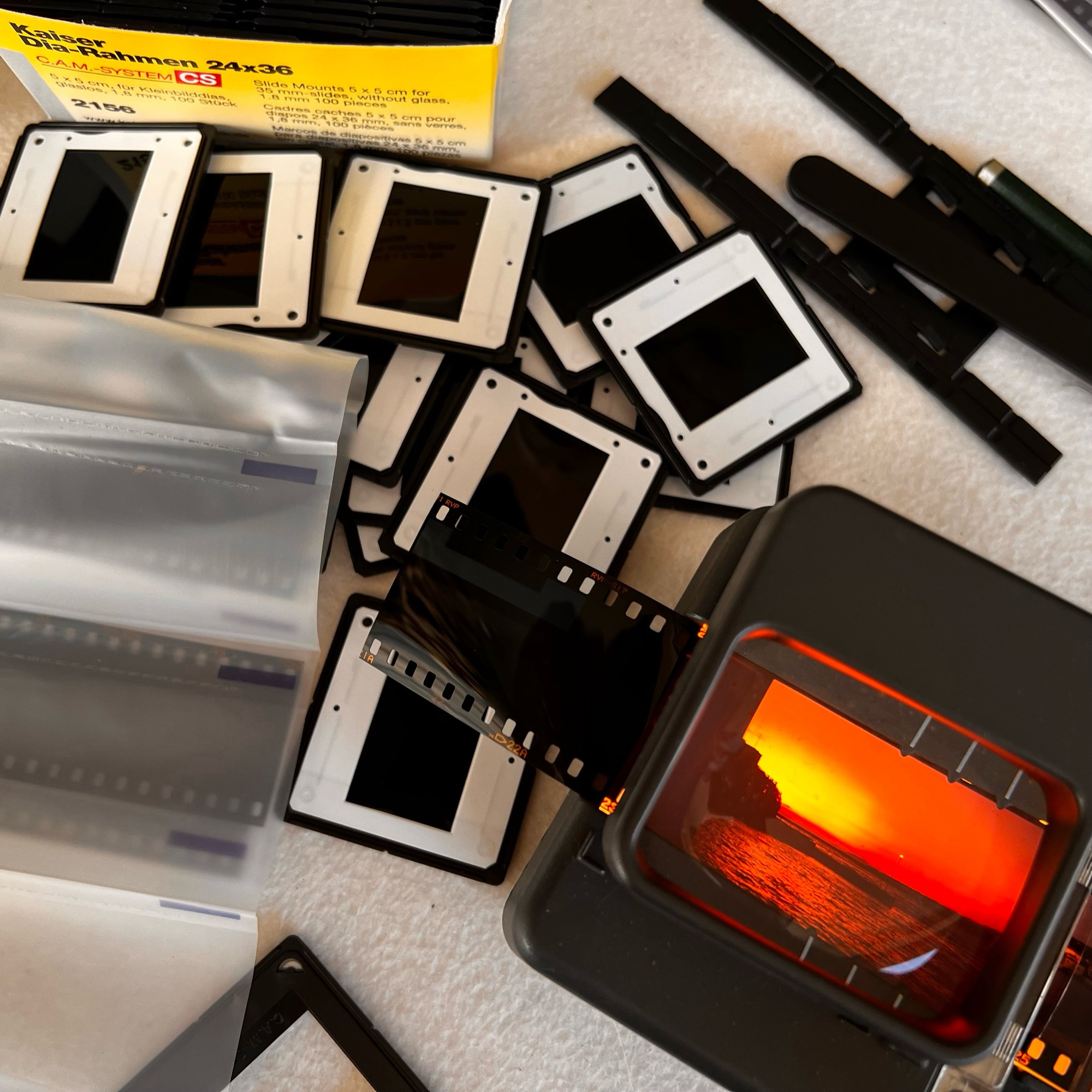 A slide showing an orange sunset is lit up on a slide cutter, next to a litter of  newly framed slides…