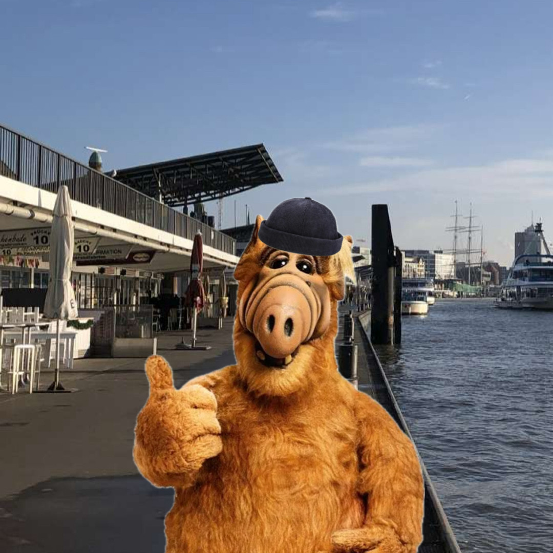 Alf mit einem Fischermütze. Im Hintergrund sind die Landungsbrücken, Hamburg