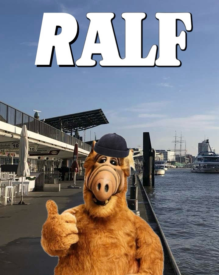 Alf mit einer Fischermütze. Im Hintergrund sind die Landungsbrücken, Hamburg 

Oben steht statt Alf Ralf