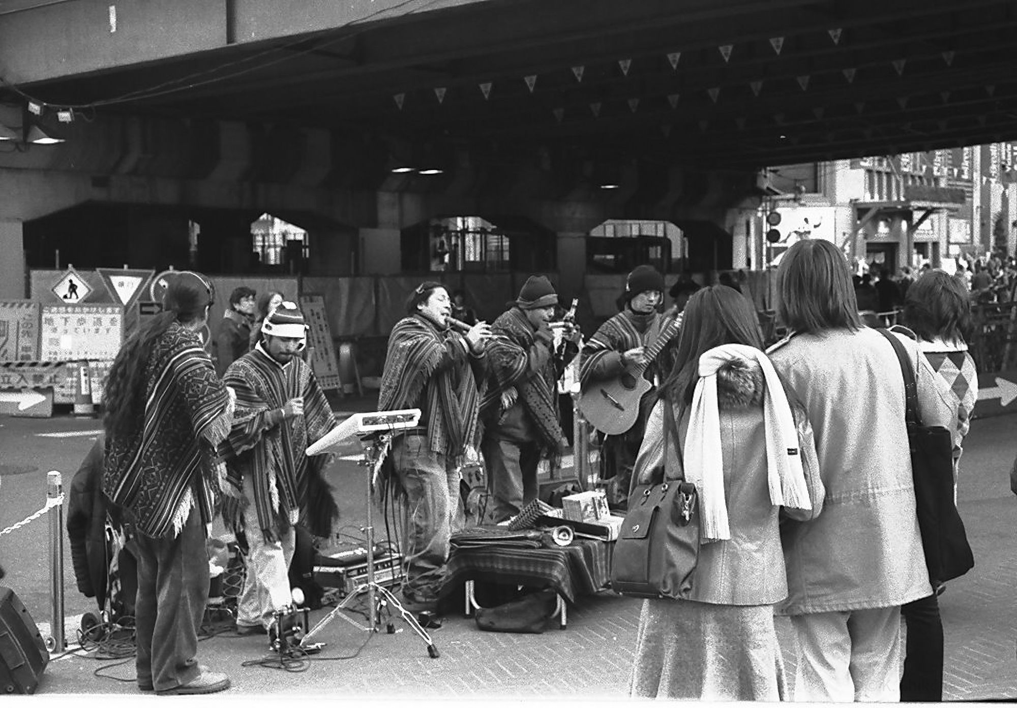 *English explanation is below*
モノクロ写真。2006年　モノクロフィルムで撮影後スキャンしたもの。

新宿駅脇、甲州街道のガード下で演奏をするフォルクローレバンド。左奥で演奏している彼らを右手前で３人の女性が聴いている。この後彼らはCDを彼女達に売り始める。一時期よくみた光景。

---

Black and white photo. Scanned after shooting with monochrome film in 2006.

A folclore band playing under the elevated road of "Koshu Kaido", next to Shinjuku Station. They are playing in the back left, and three women are listening in front of them on the right.
After this, they start selling CDs to them. A scene that I often saw for a while.