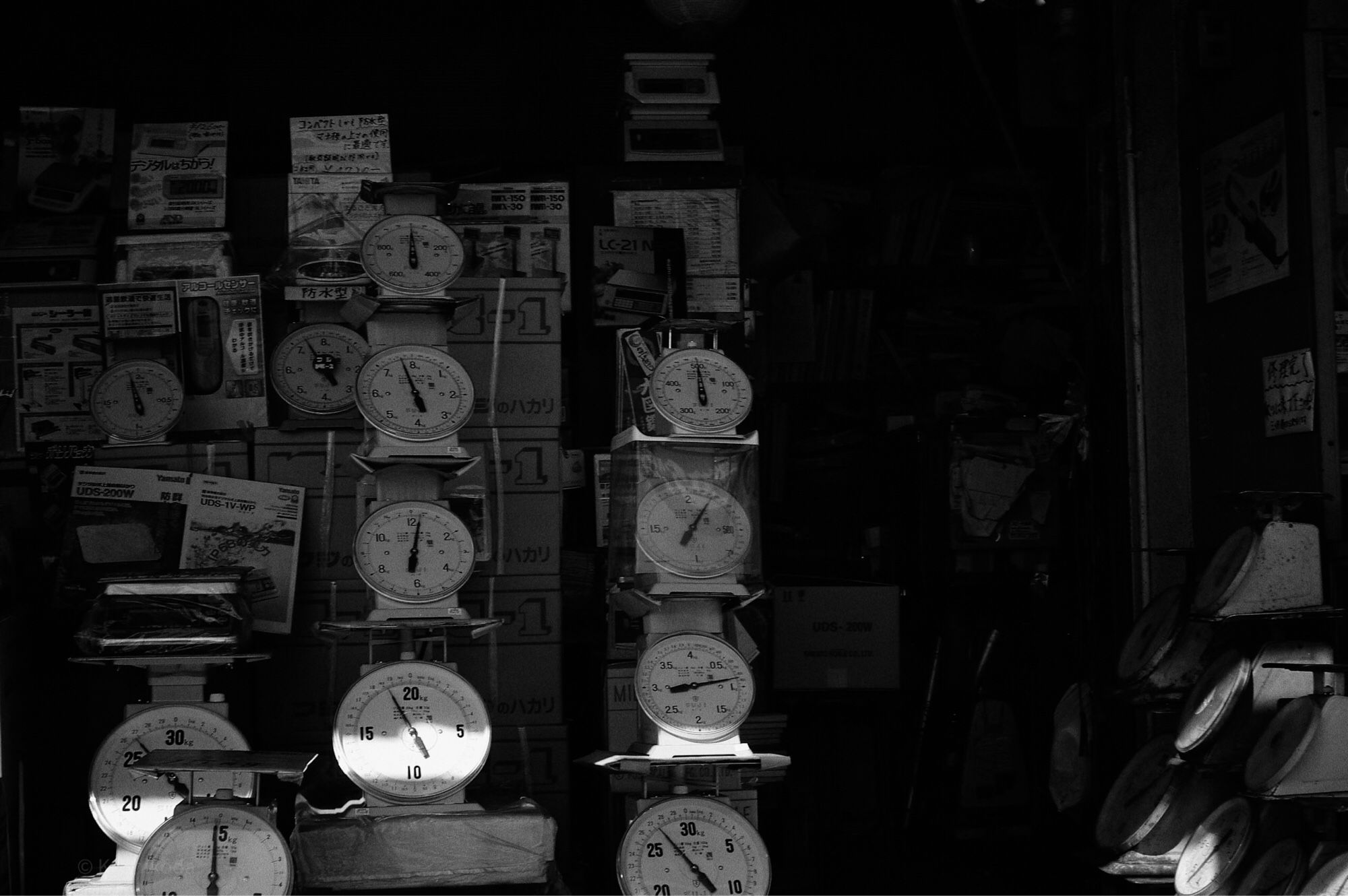 Black and white photo
The outer market of "Tsukiji Market”, known as «Tokyo's kitchen», not only sold fresh fish and other ingredients, but also processed food products, and there were many stores selling professional tools for the people who worked there. Scales, which weigh items by placing them on them, were no exception. Scales of all sizes were lined up in the storefronts, and light was filtering through some of them. Photo taken in 2007.

築地場外には中で働く人たちの道具を専門に扱うお店も数多くあり、この秤専門店も例外ではない。所狭しと陳列されている店頭に、僅かに差し込む光を捉えた。2007年撮影。