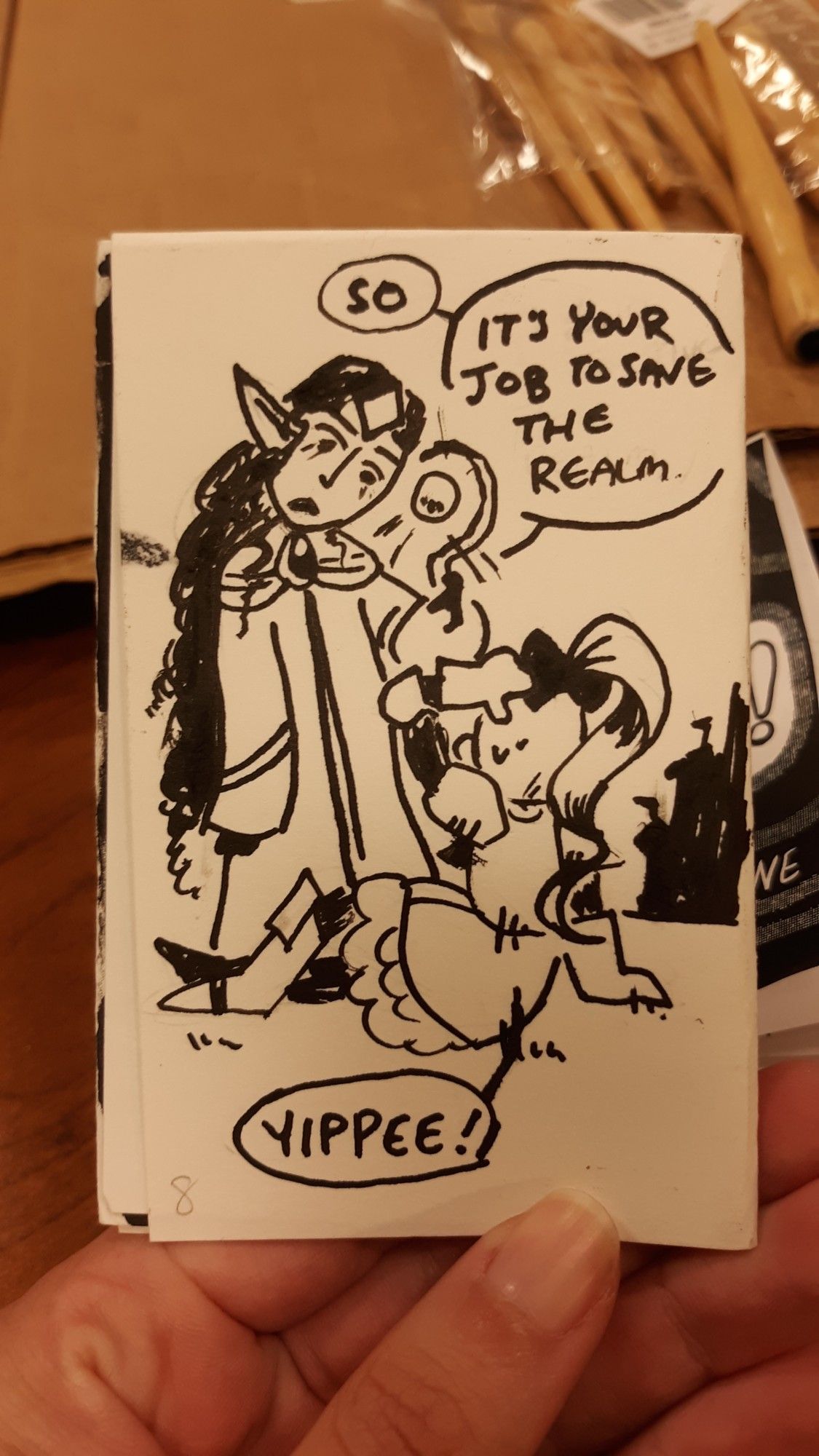 Photograph of a traditional zine. Page 7: A fancy elf holding a staff says "So. It's your job to save the realm." The girl is seen from behind, sitting up. She says, "yippee."