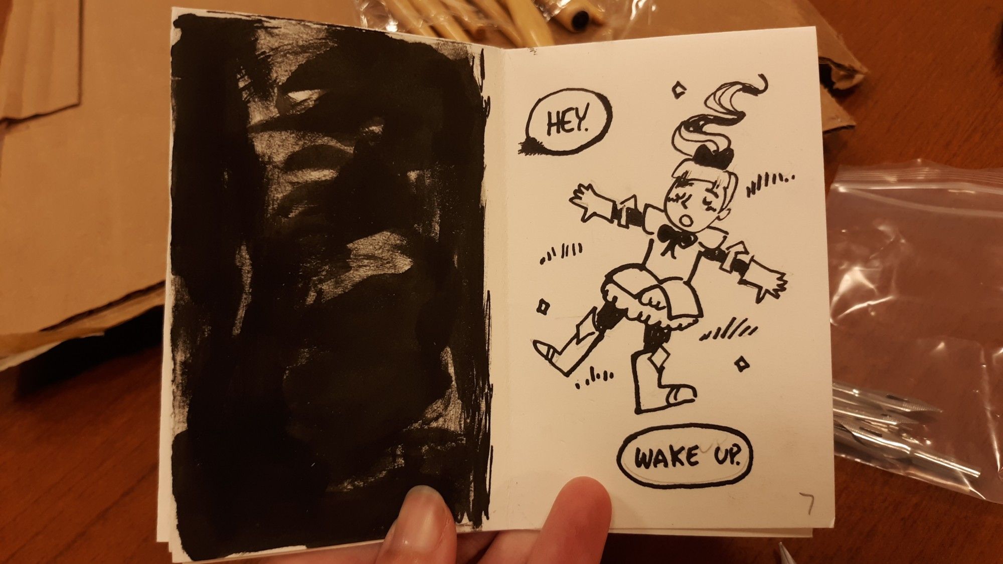 Photograph of a traditional zine. Page 5: blacked out. Page 6: The girl is wearing fancy armor and is sprawled in a field. Word balloons say "Hey. Wake up."