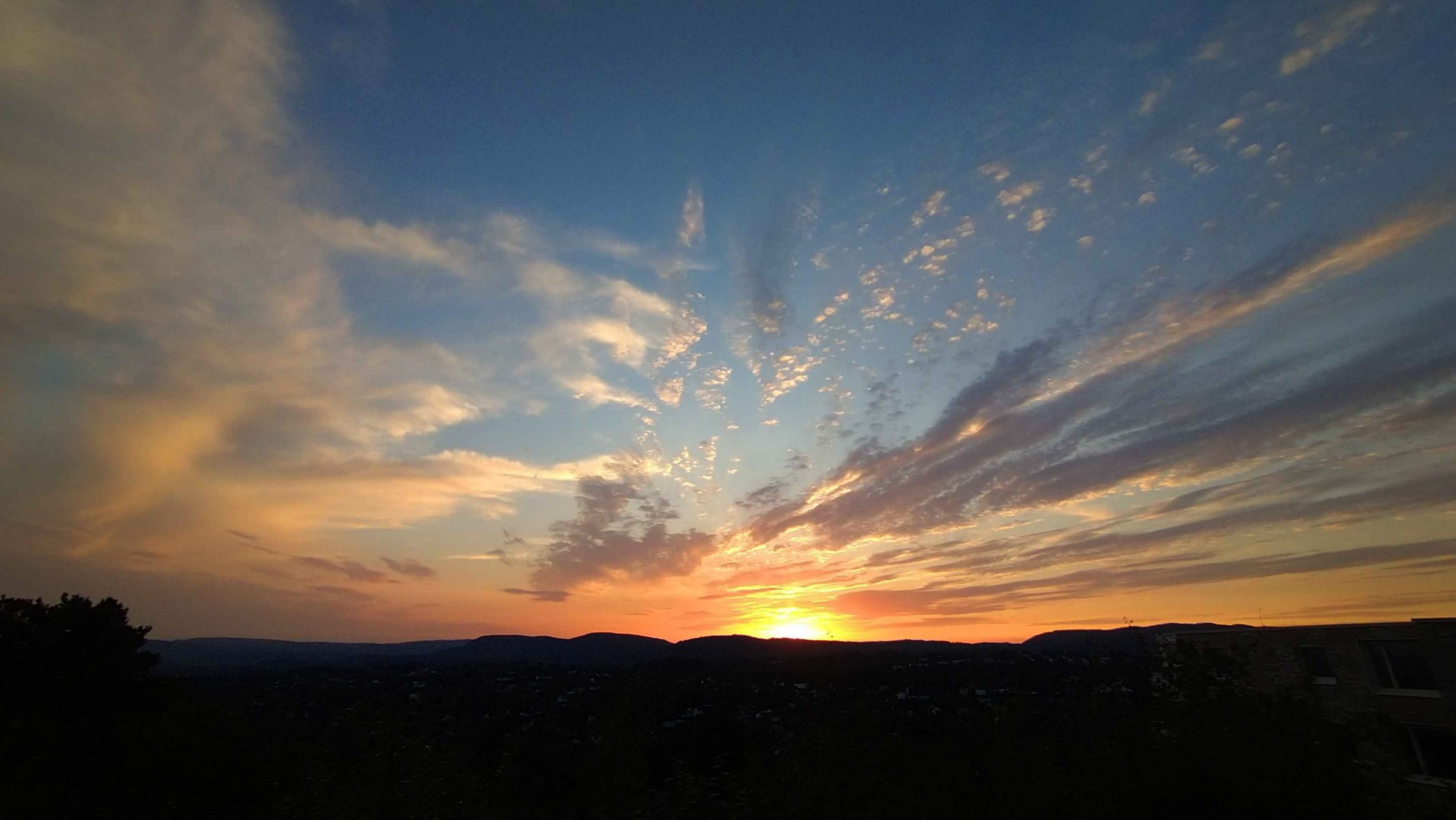 A sunset in an orange-blue sky over a dark backdrop of hills