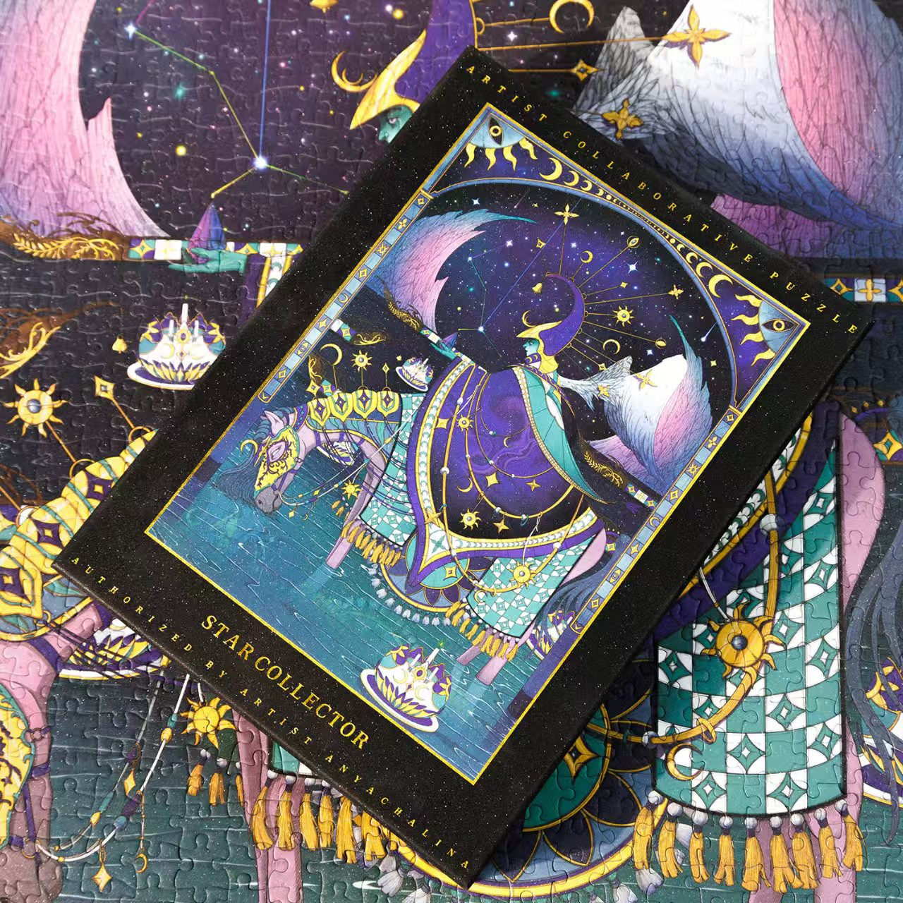 A picture of the puzzle box with my artwork "Star Collector". The artwork shows a person in a decorated cape and a hat riding a horse while standing in the shallow water. There are lanterns floating on the water and pink mountains on the horizon. There's an already assembled puzzle under the box.