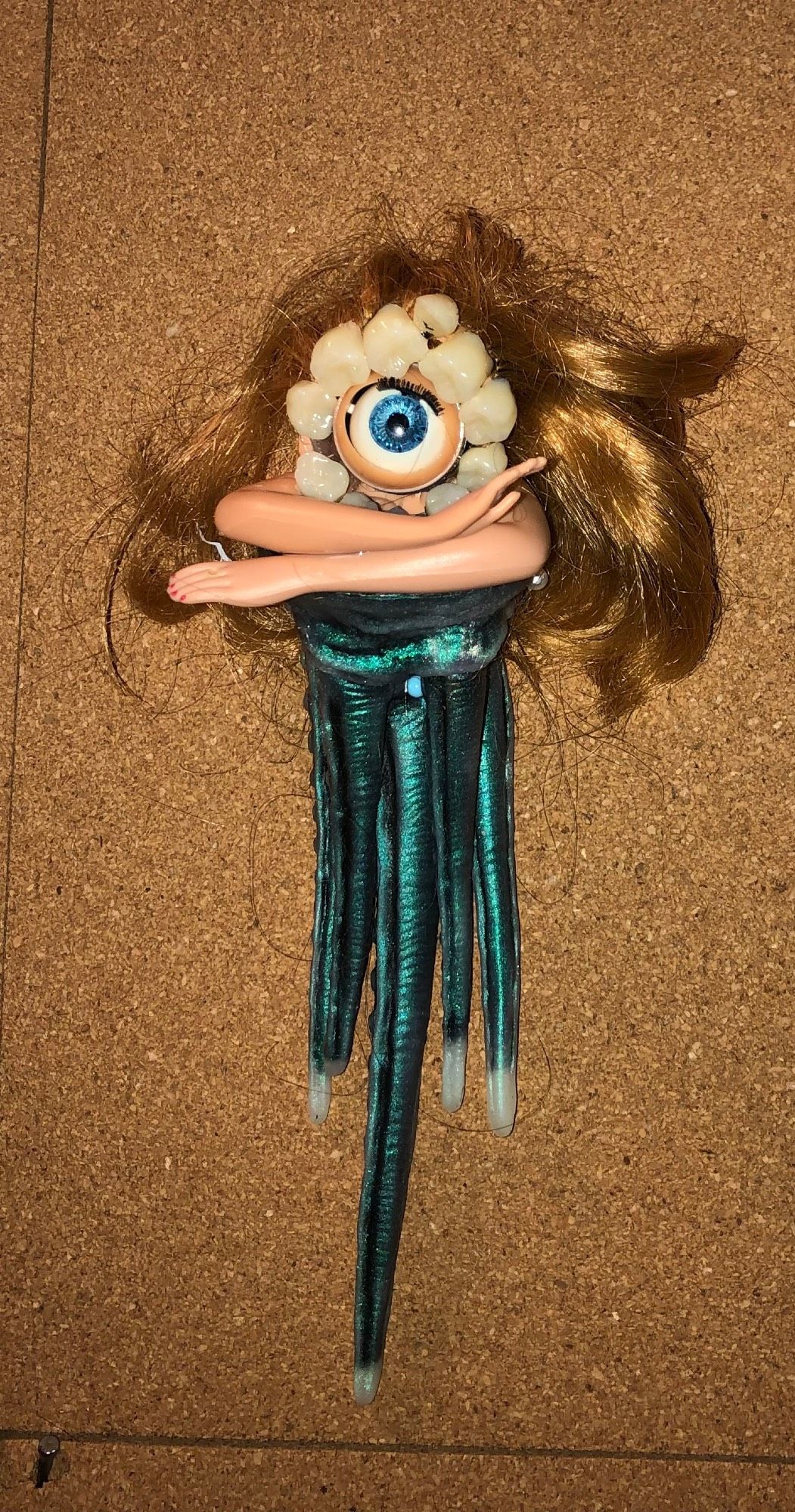 rubbery tentacles beneath a large blue (blinky) eye. the wye has a honey blond wig and a halo or teeth.  two arms in the "speak to the hand pose"