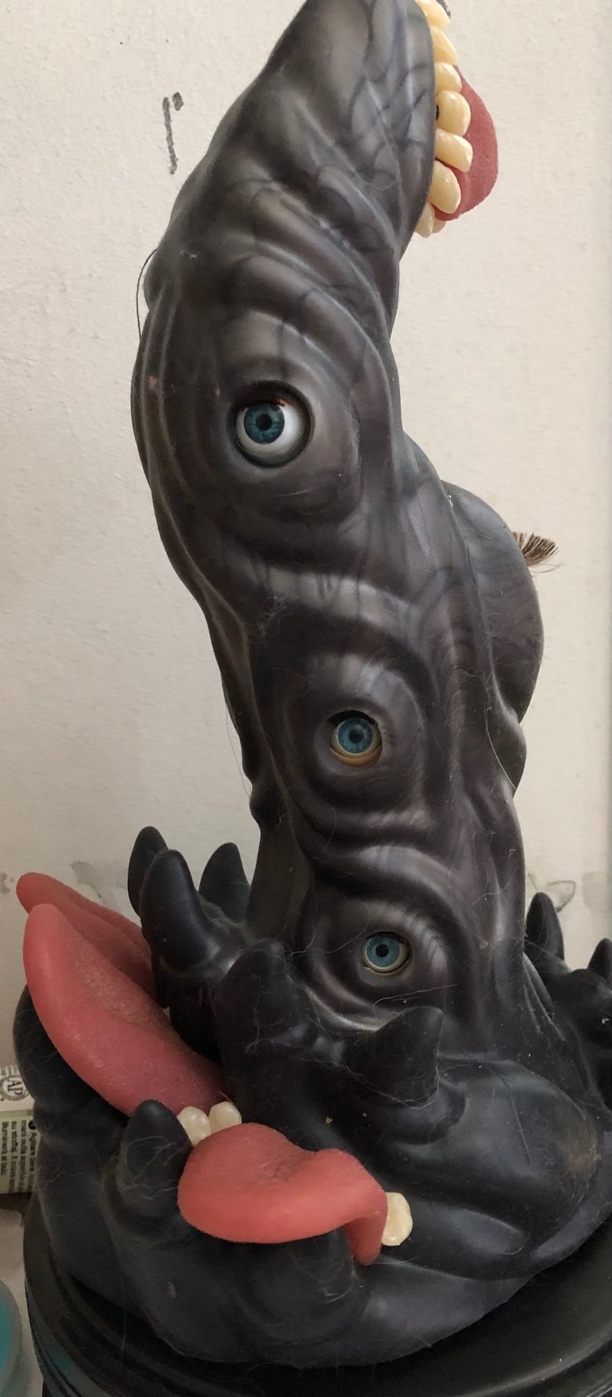 close up of a dark green grey tentacle like item with teeth, eyes and tongues