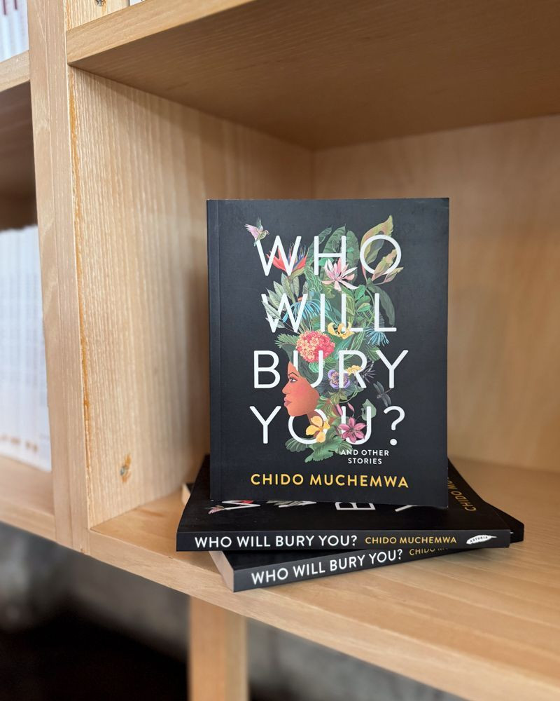 The book WHO WILL BURY YOU sits on a wooden shelf.